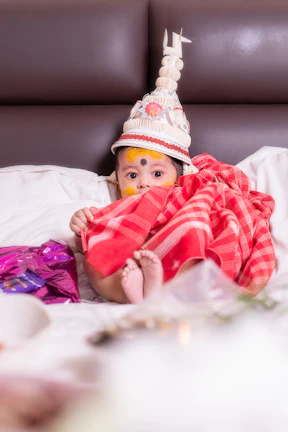 A baby dressed in traditional attire sits on a bed.