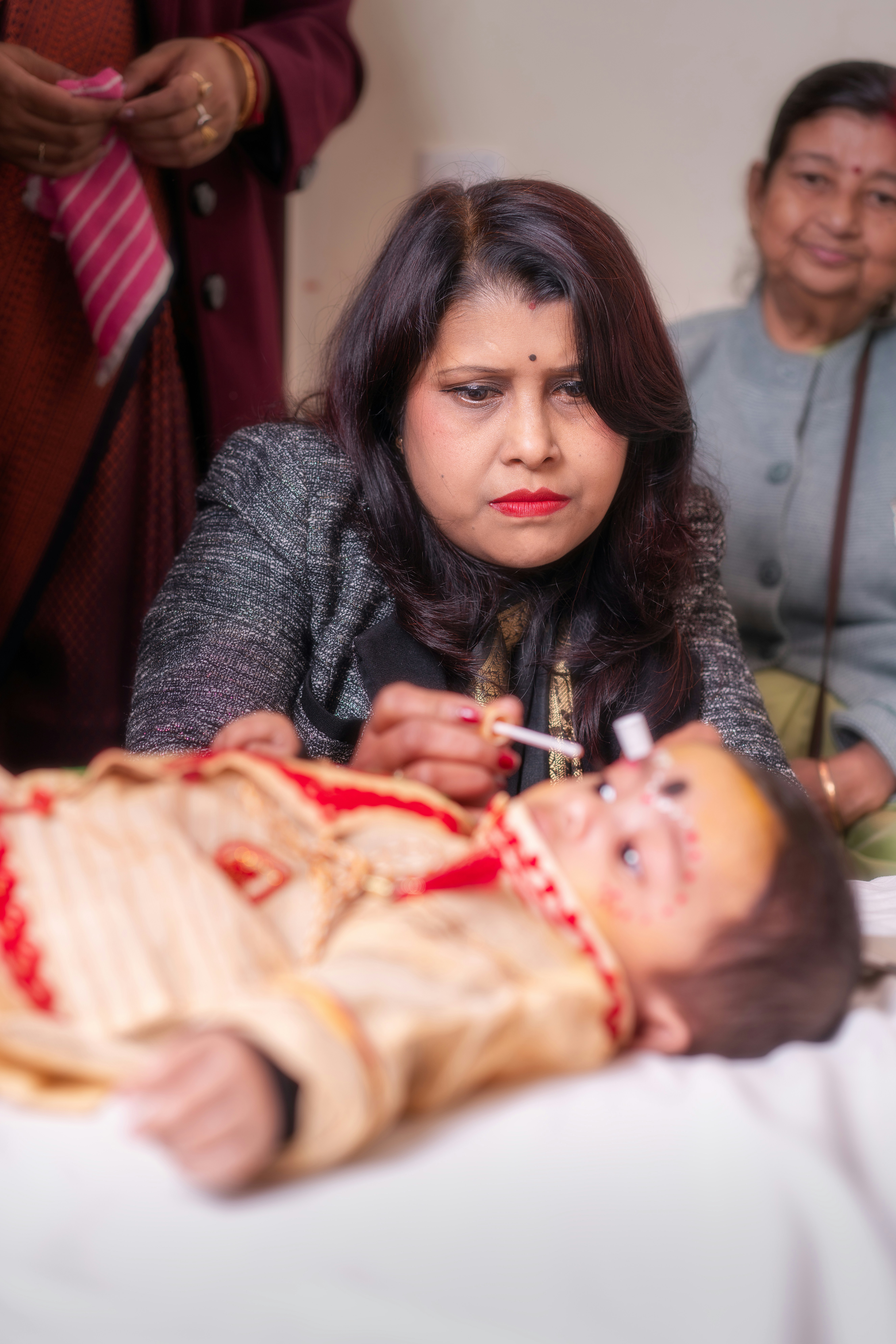 Woman applying makeup to a baby in traditional attire.