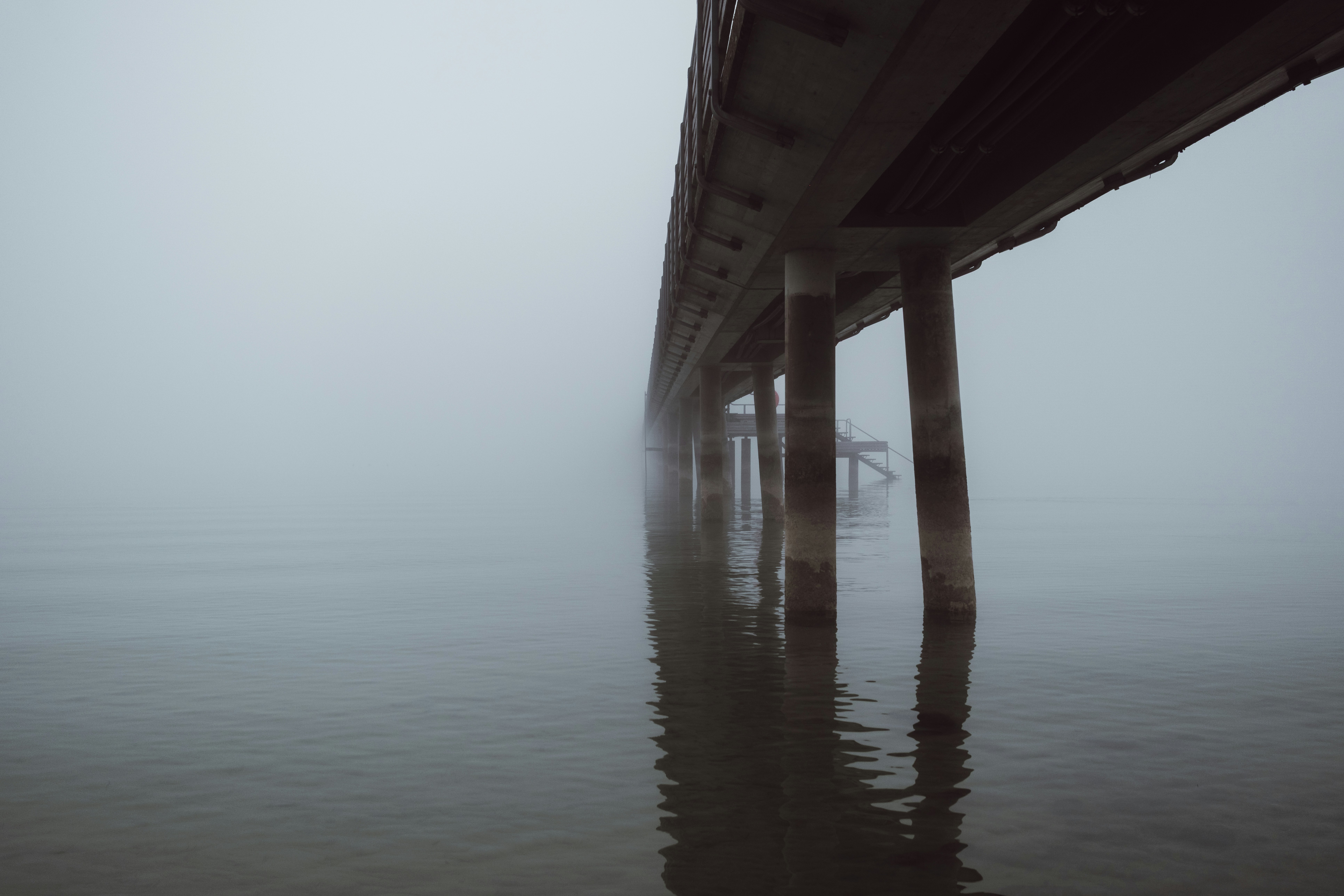 A bridge pier disappearing into thick fog over water.