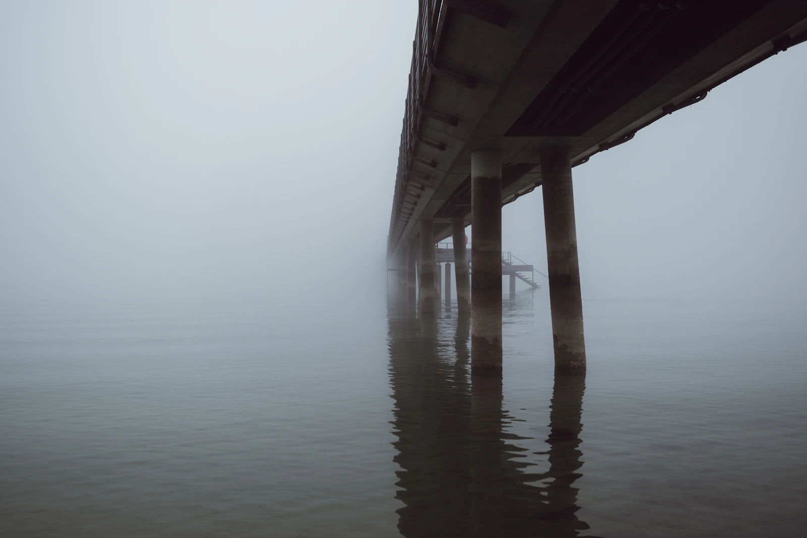 A bridge pier disappearing into thick fog over water