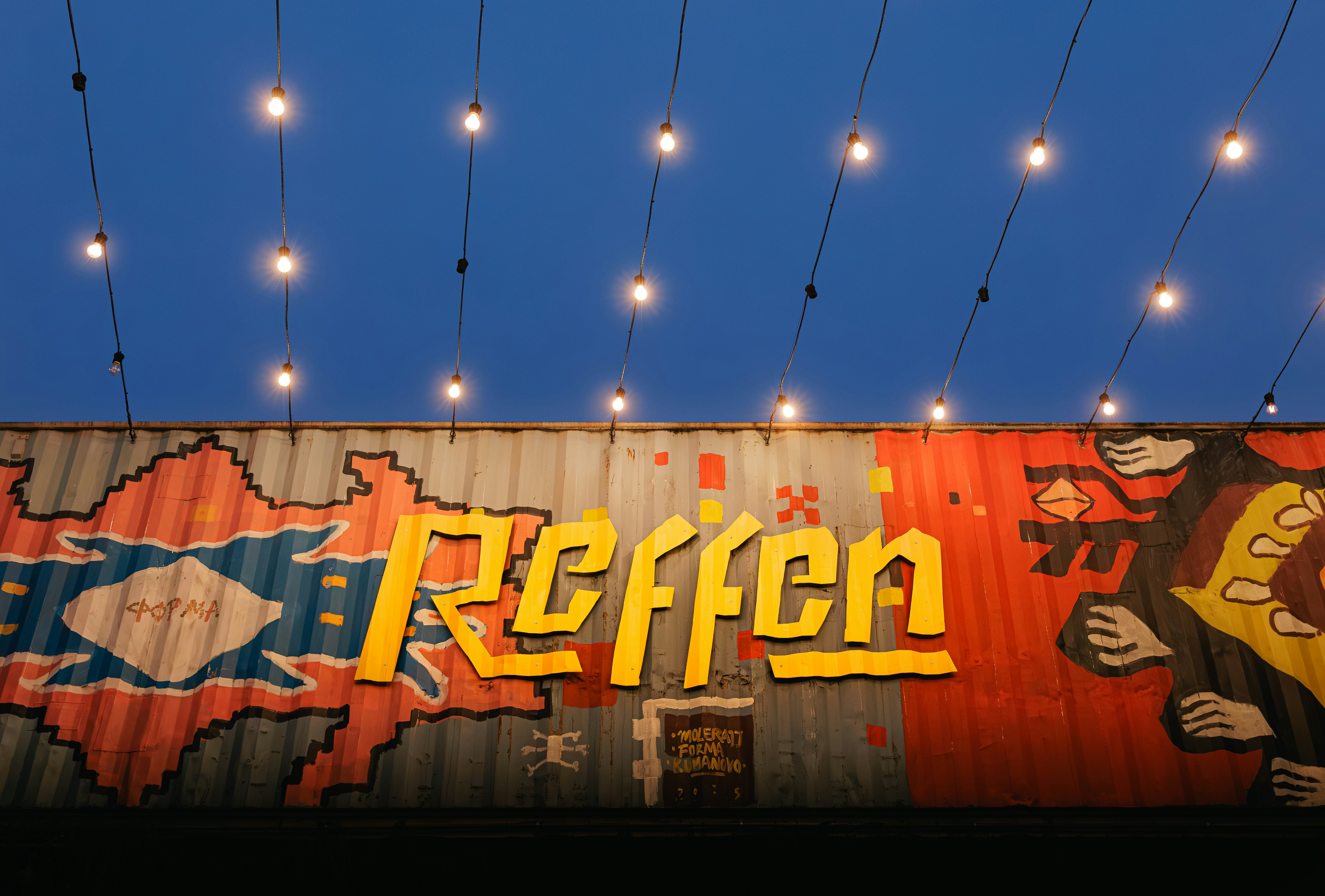 Graffiti art on a corrugated metal wall with string lights.