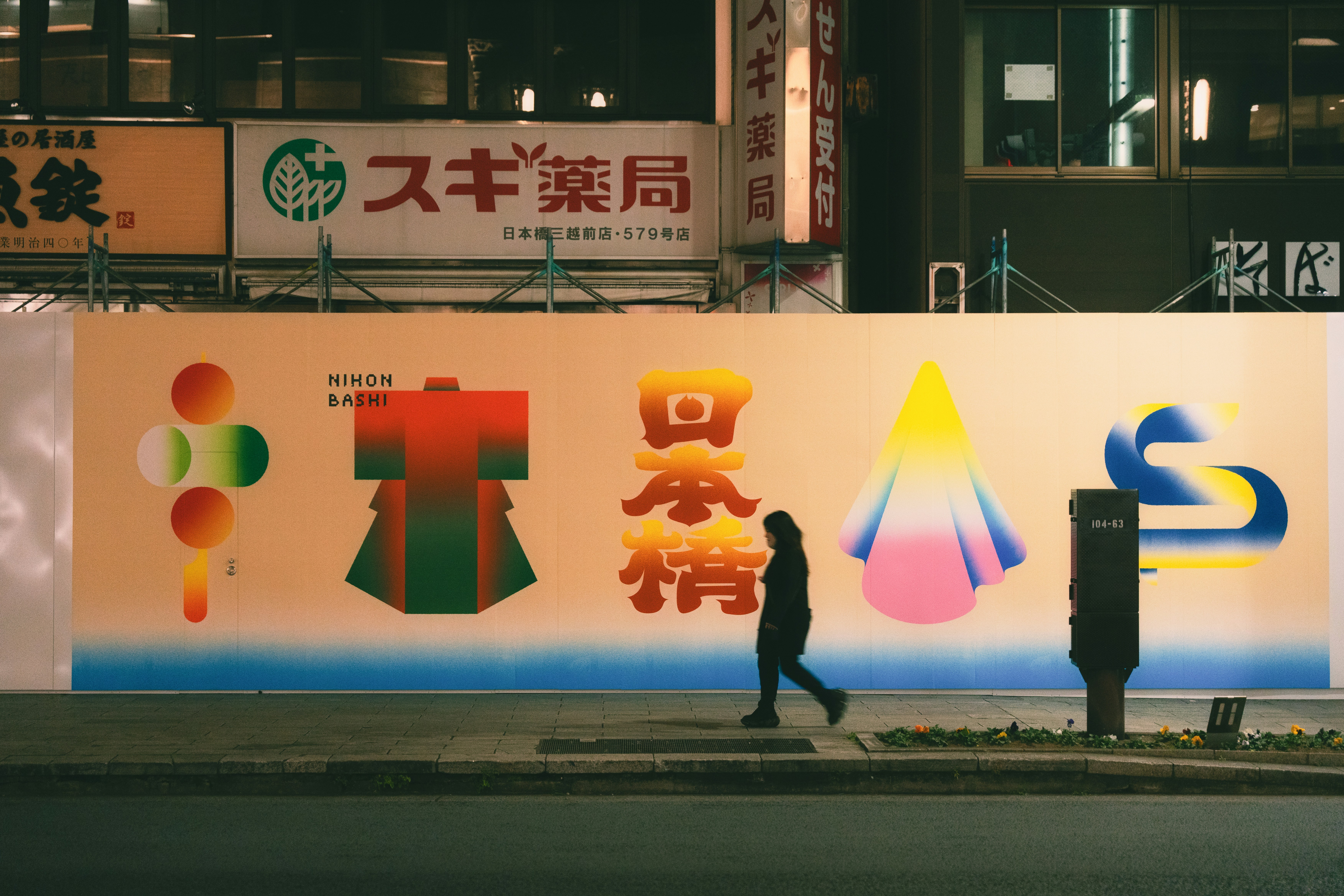 Person walks past colorful mural on city street at night