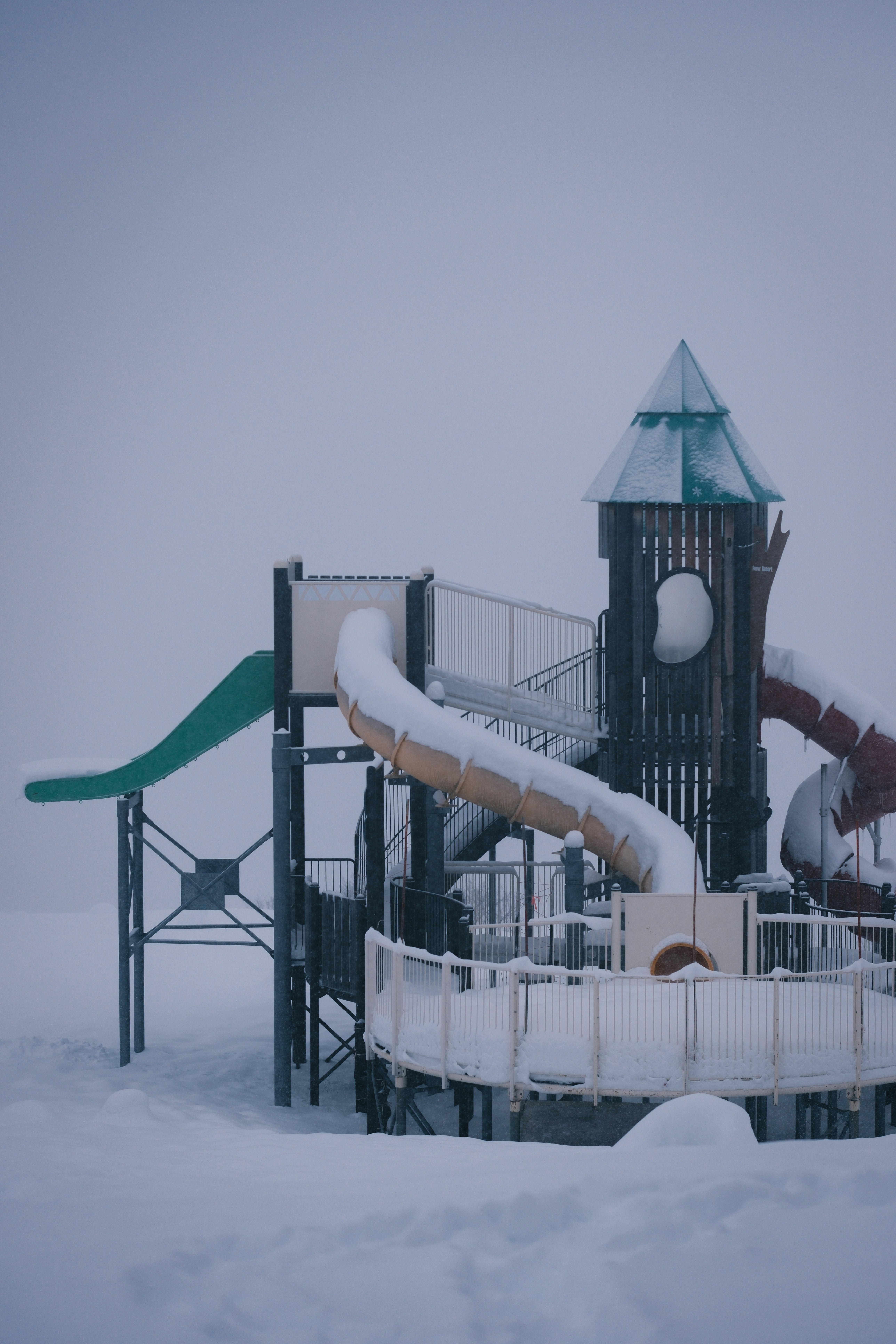 Snow-covered playground equipment on a foggy day