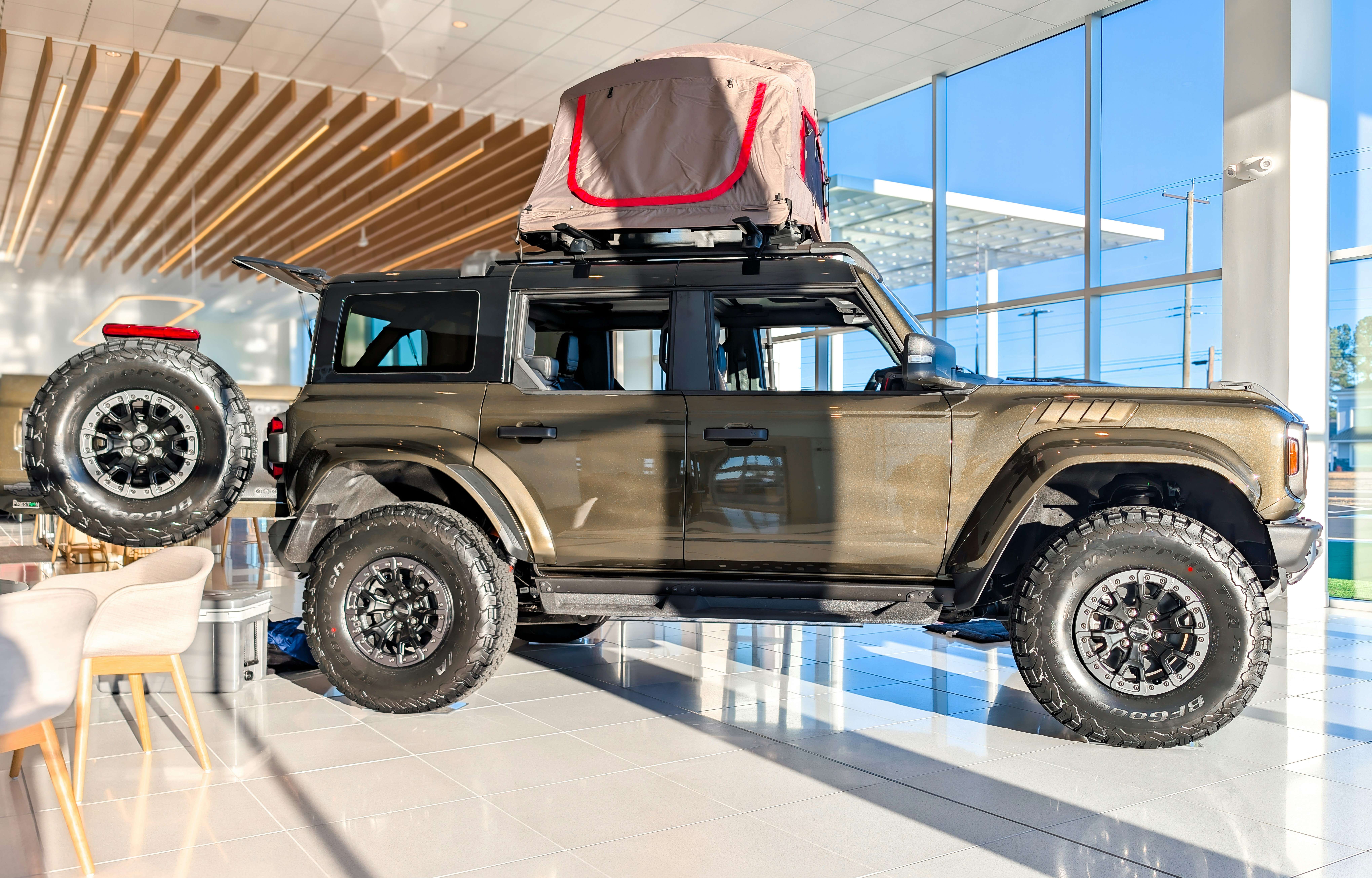 Brown off-road vehicle with rooftop tent and spare tire.