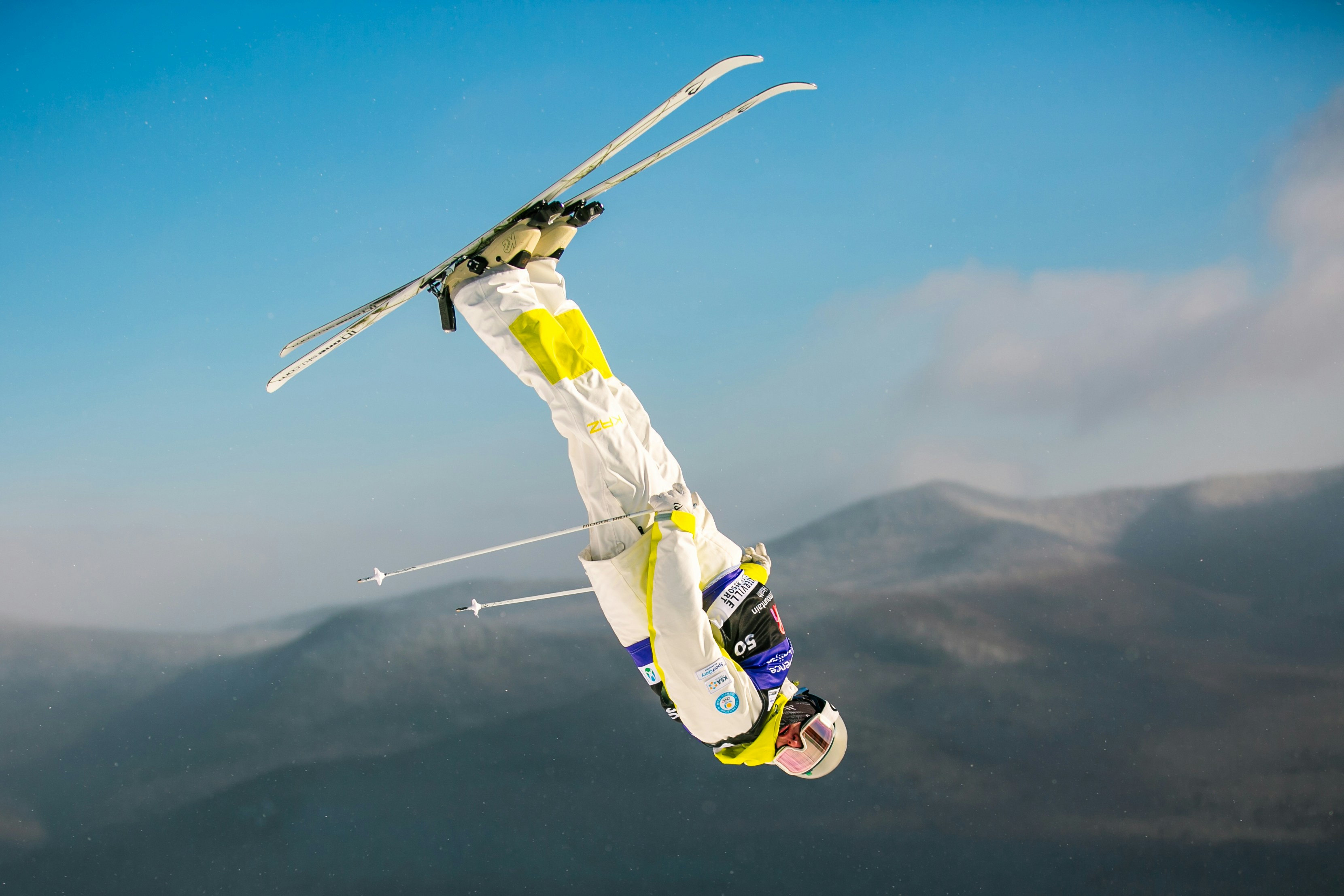 A skier performs a flip mid-air against a mountain backdrop.