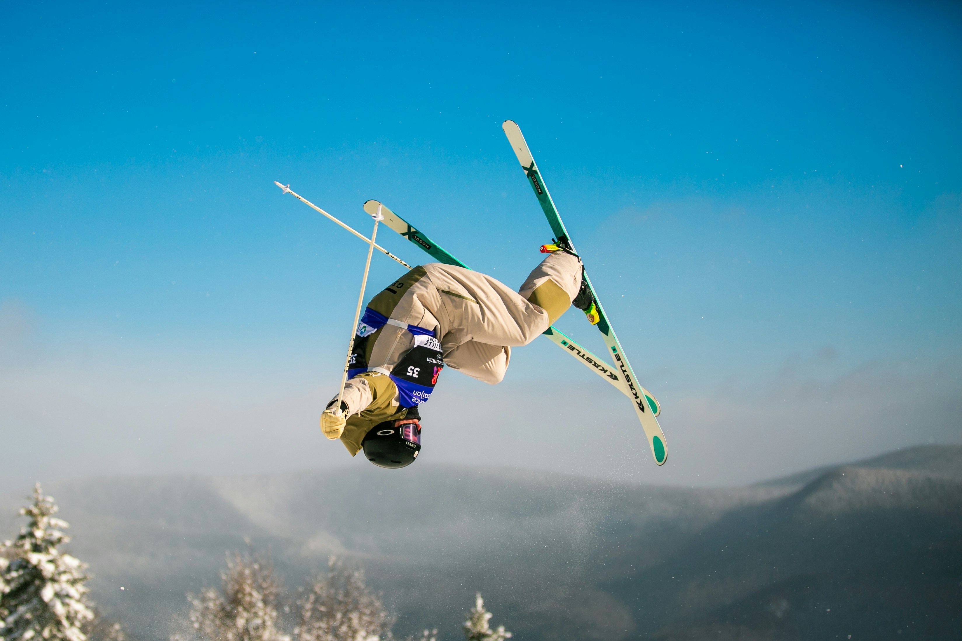 A skier performs a backflip against a clear blue sky.