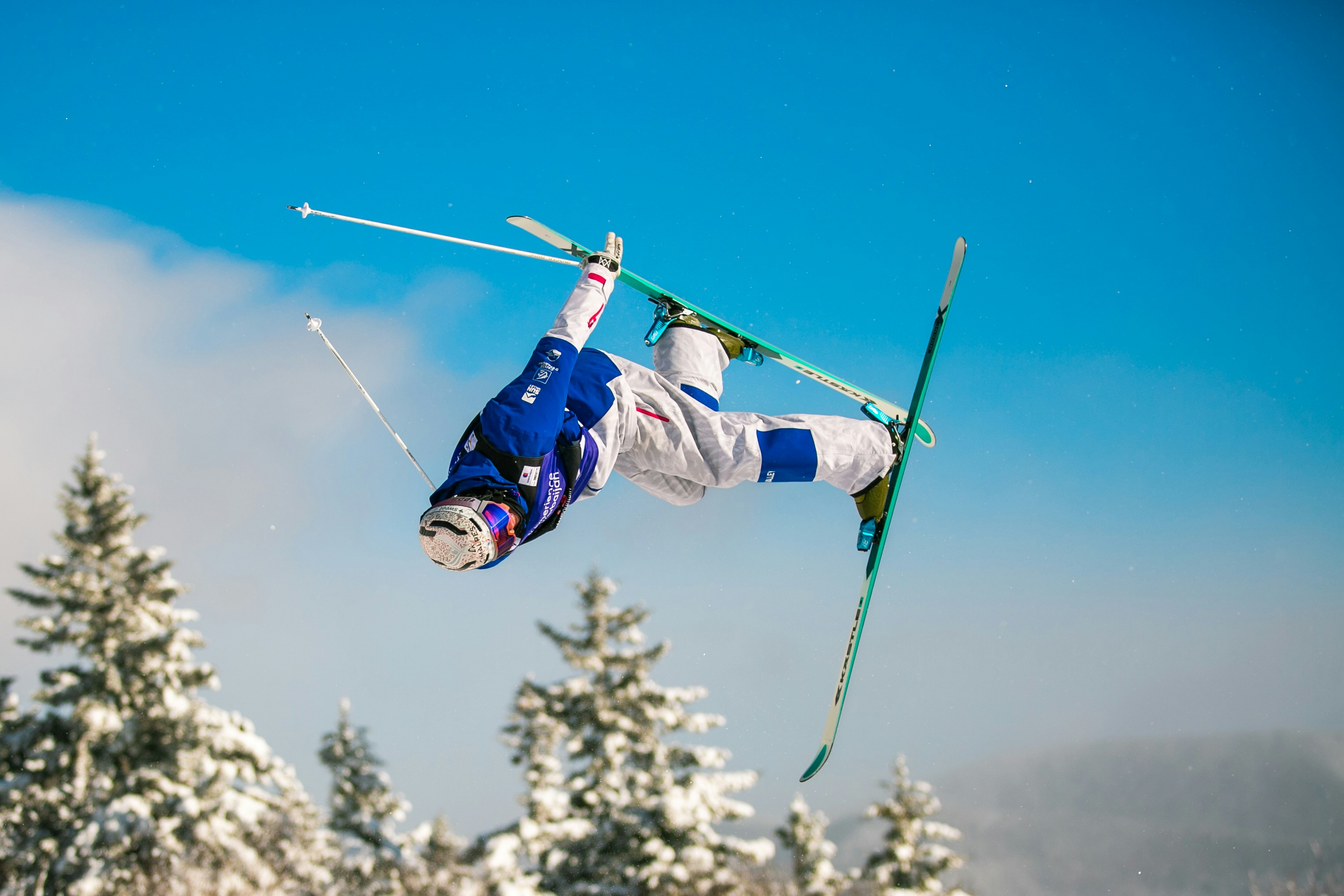 A skier performs a flip mid-air against a blue sky.