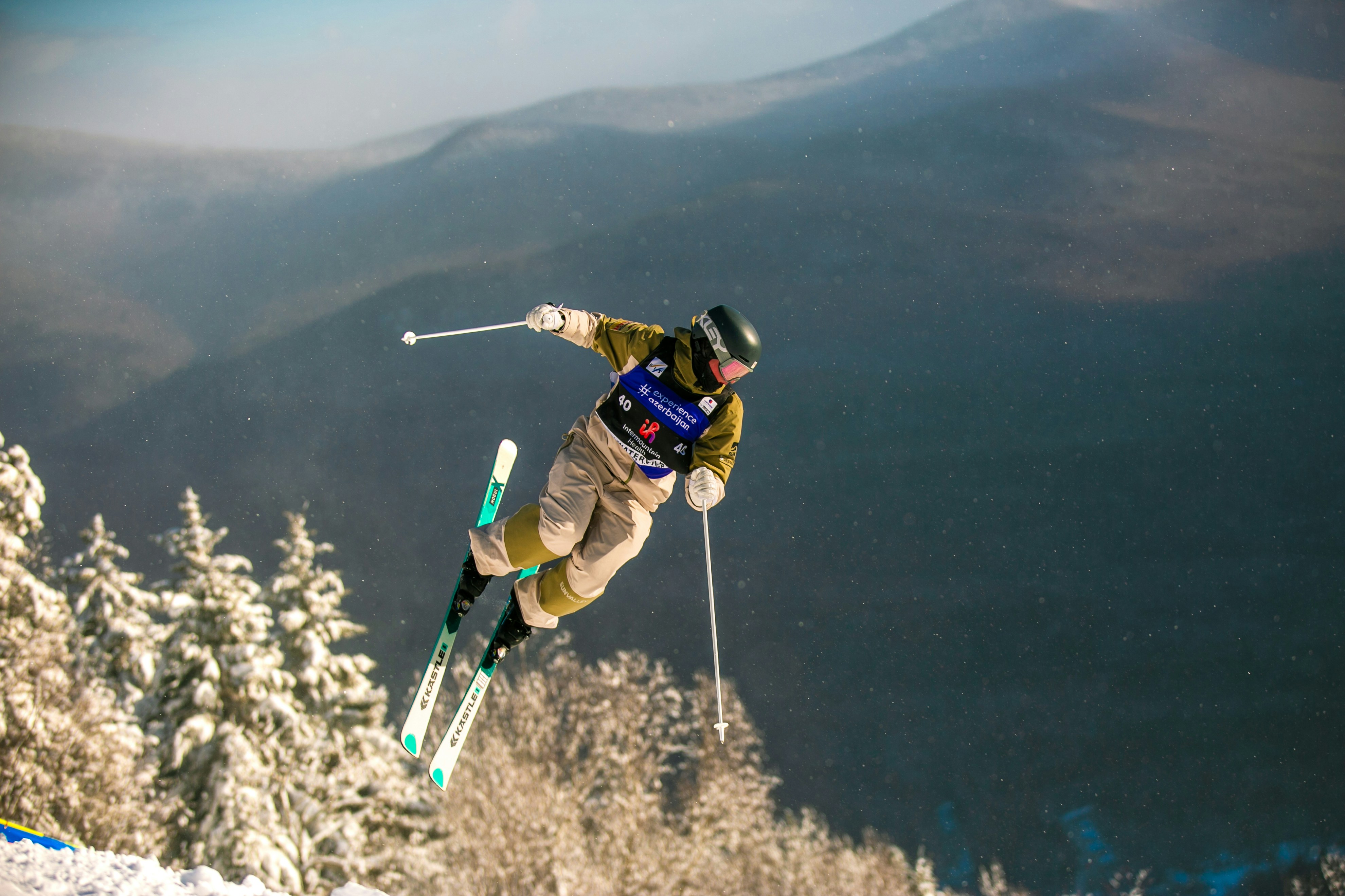 A skier performs a trick mid-air against a mountain backdrop.