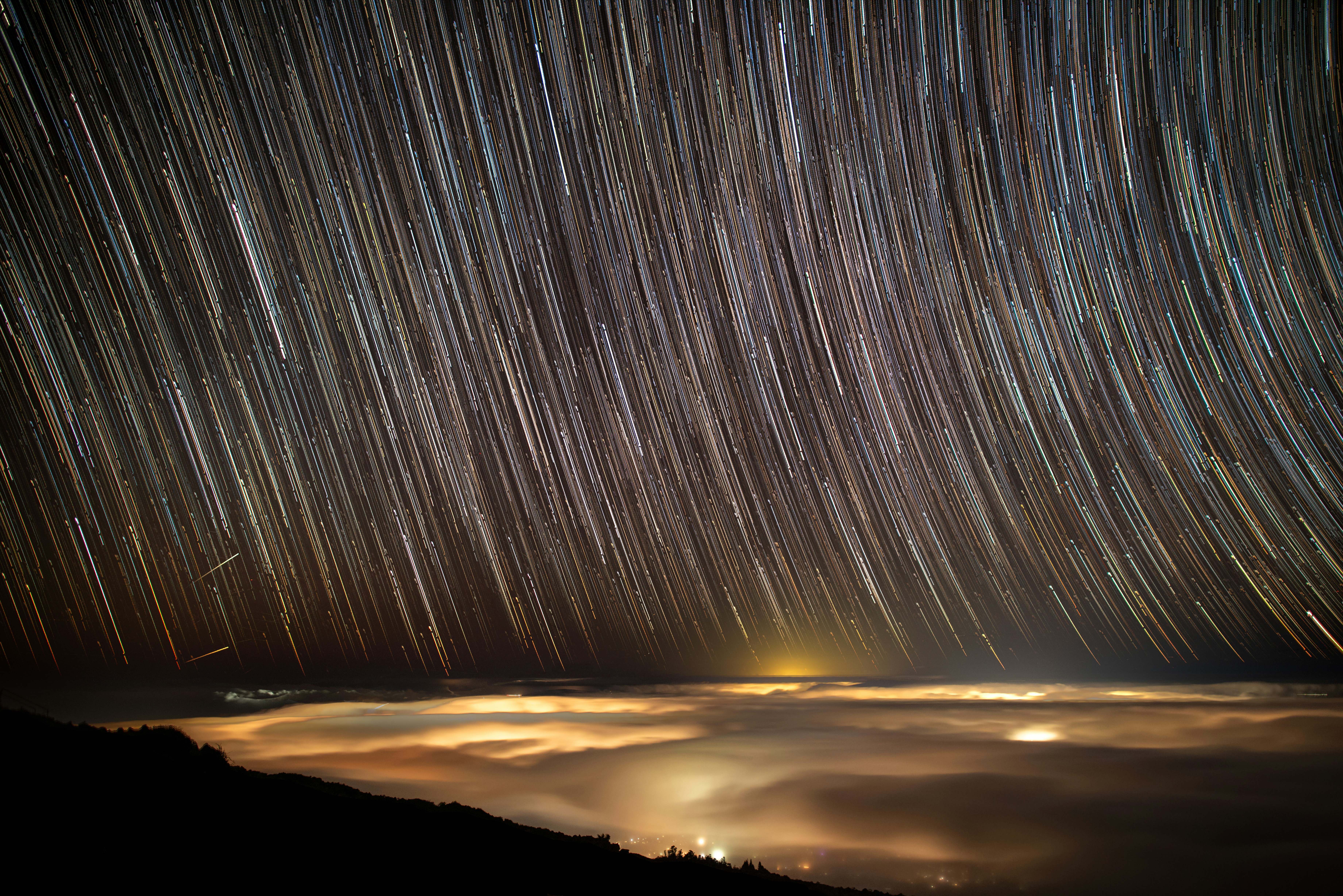 Star trails over a cloud-filled valley at night