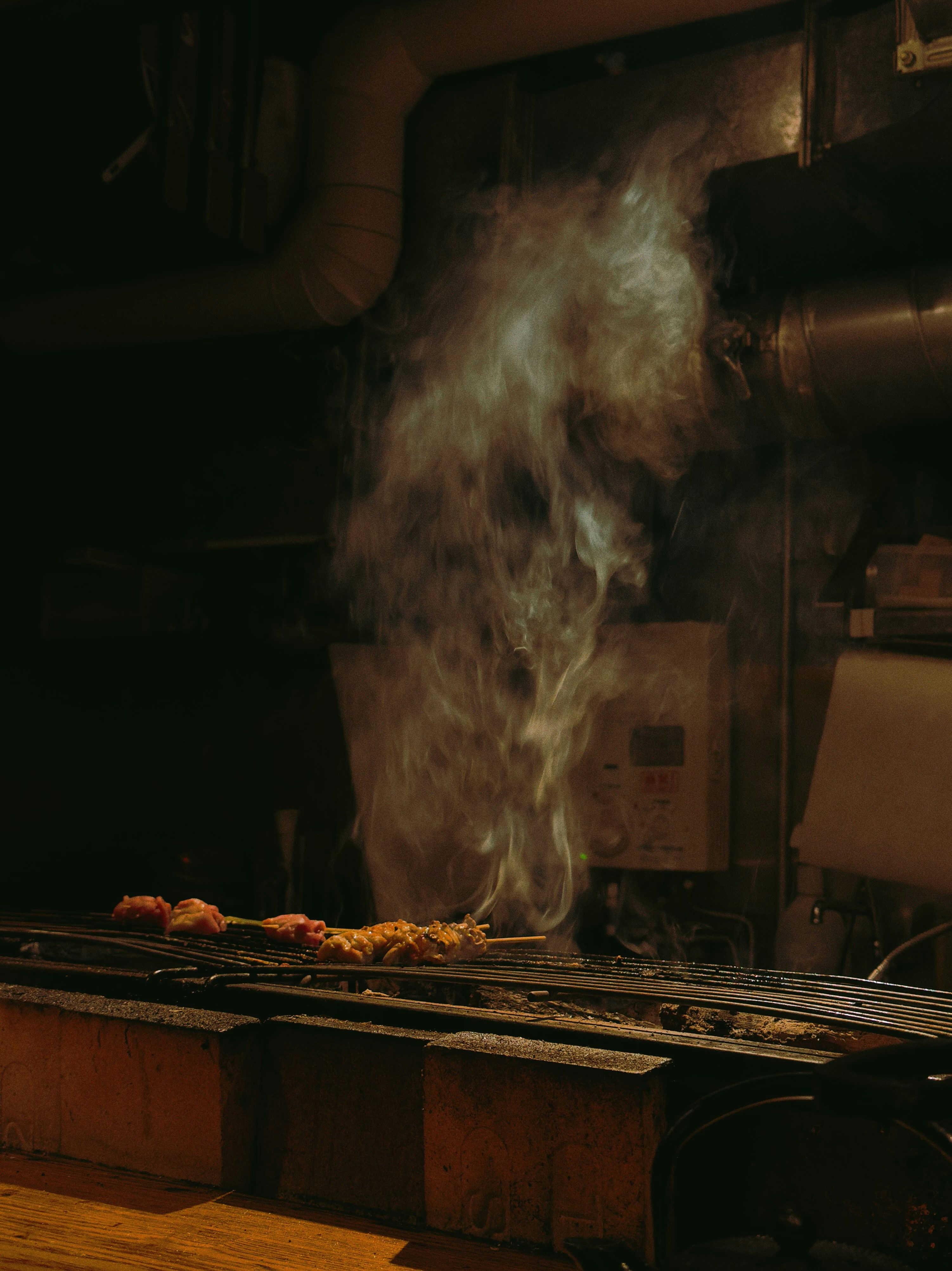 Smoke rising from skewers cooking on a grill.