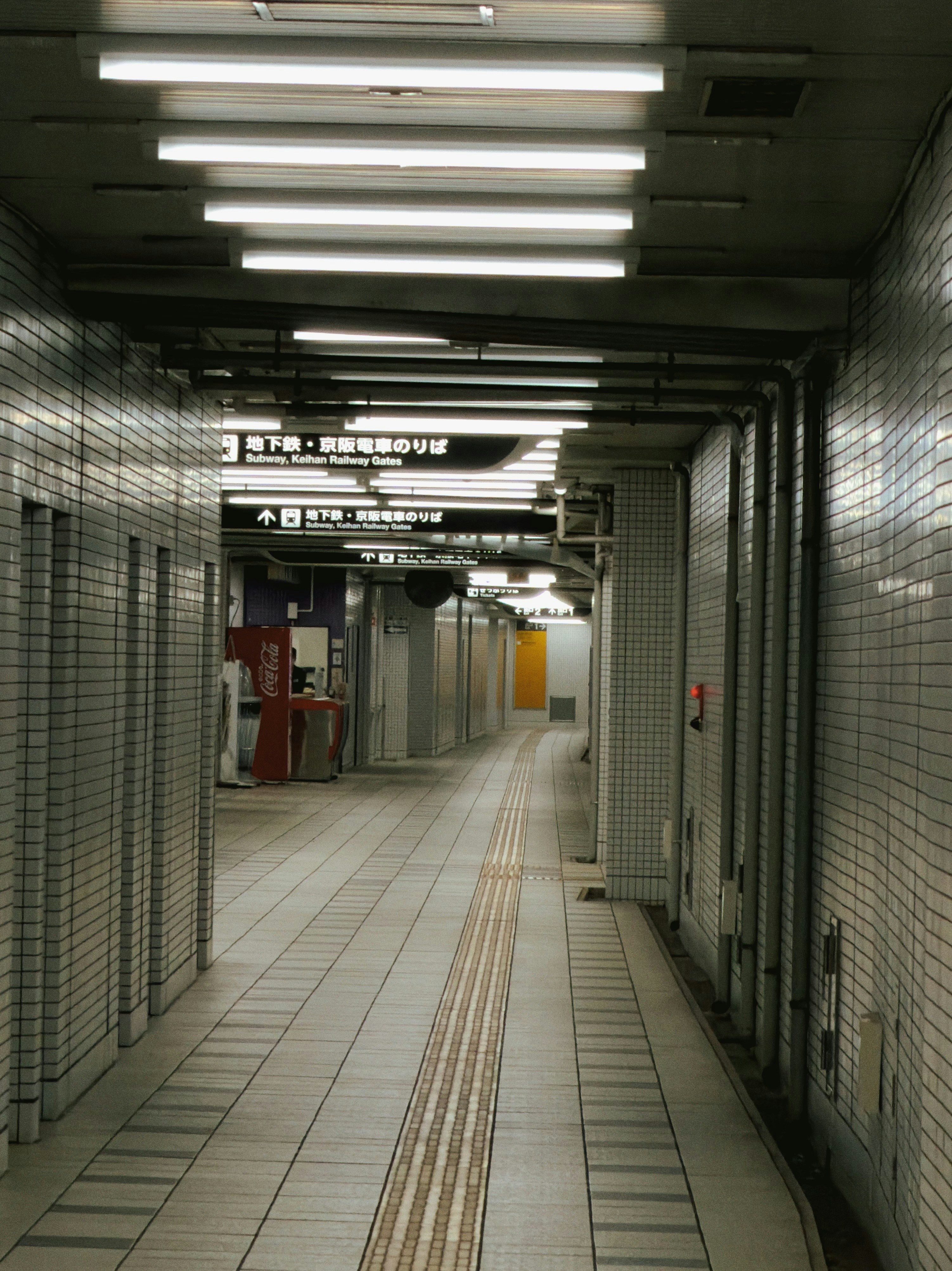 Empty subway station hallway with tiled walls and fluorescent lights.