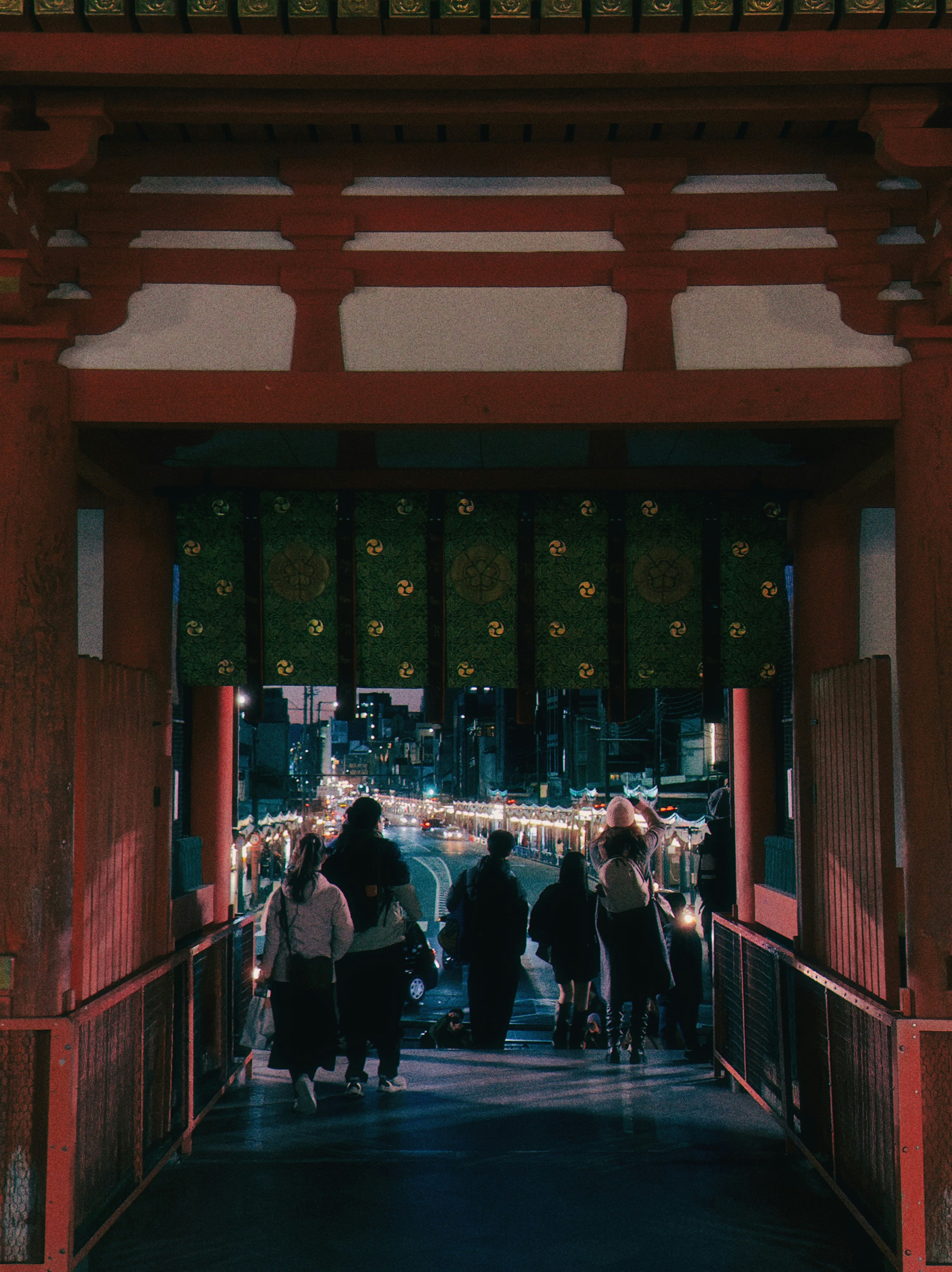 People walking through a red temple gate at night