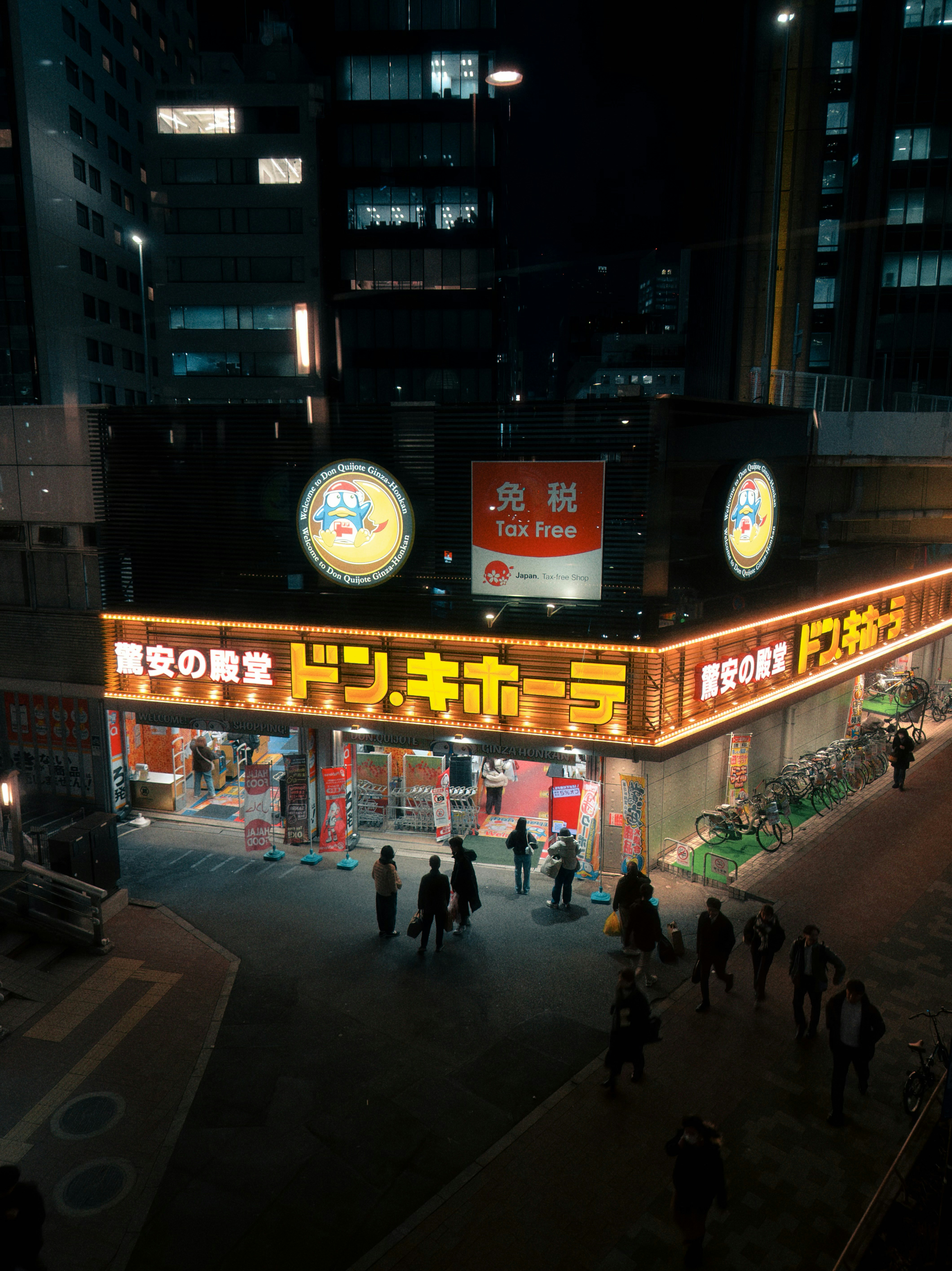 Busy street scene outside a brightly lit store at night.