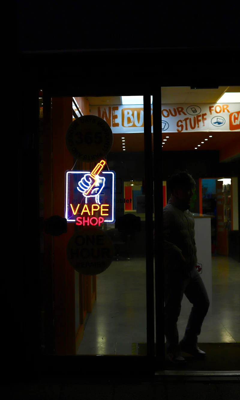 Neon vape shop sign glowing in the storefront window at night