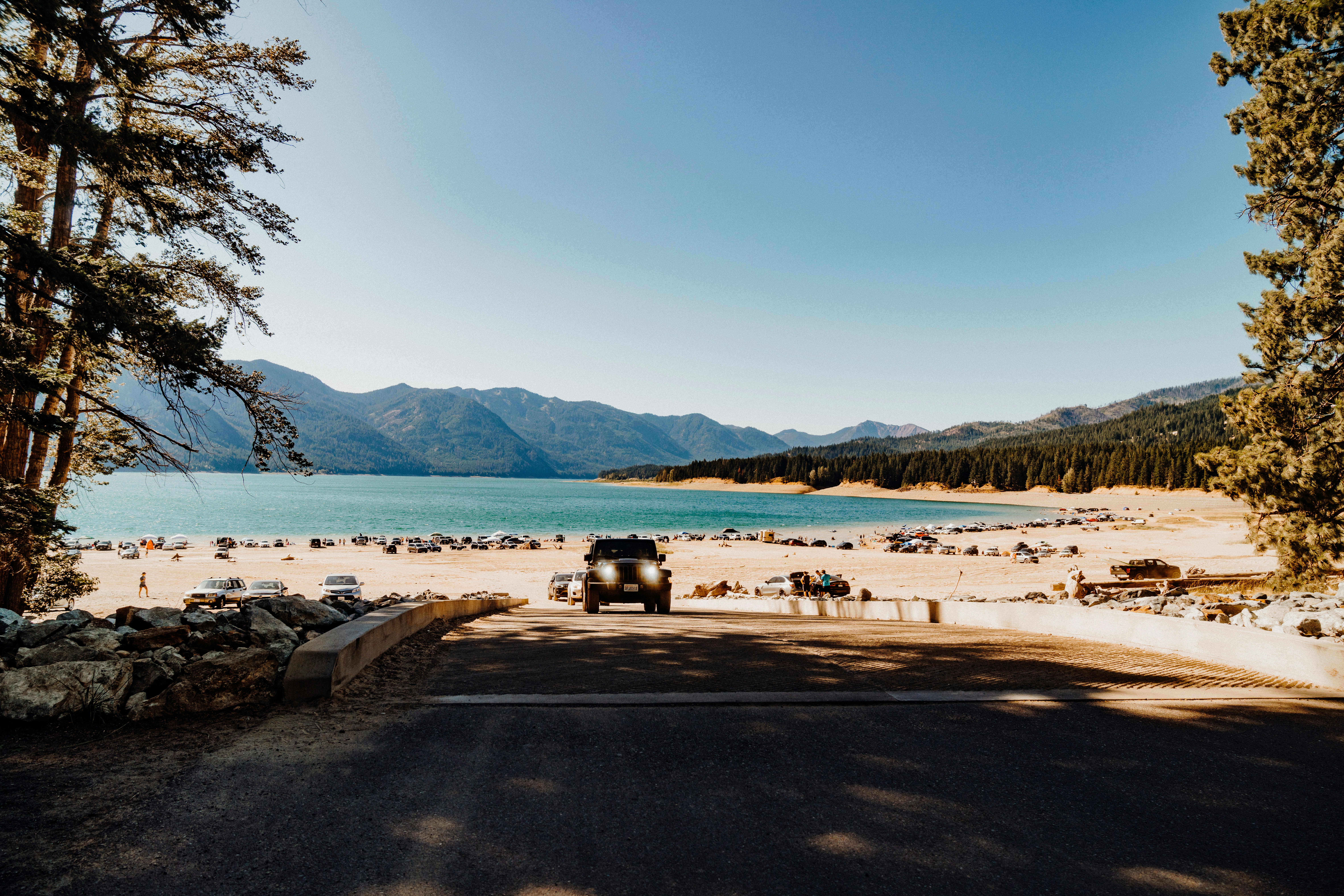 Black suv parked by a bright blue lake and mountains.
