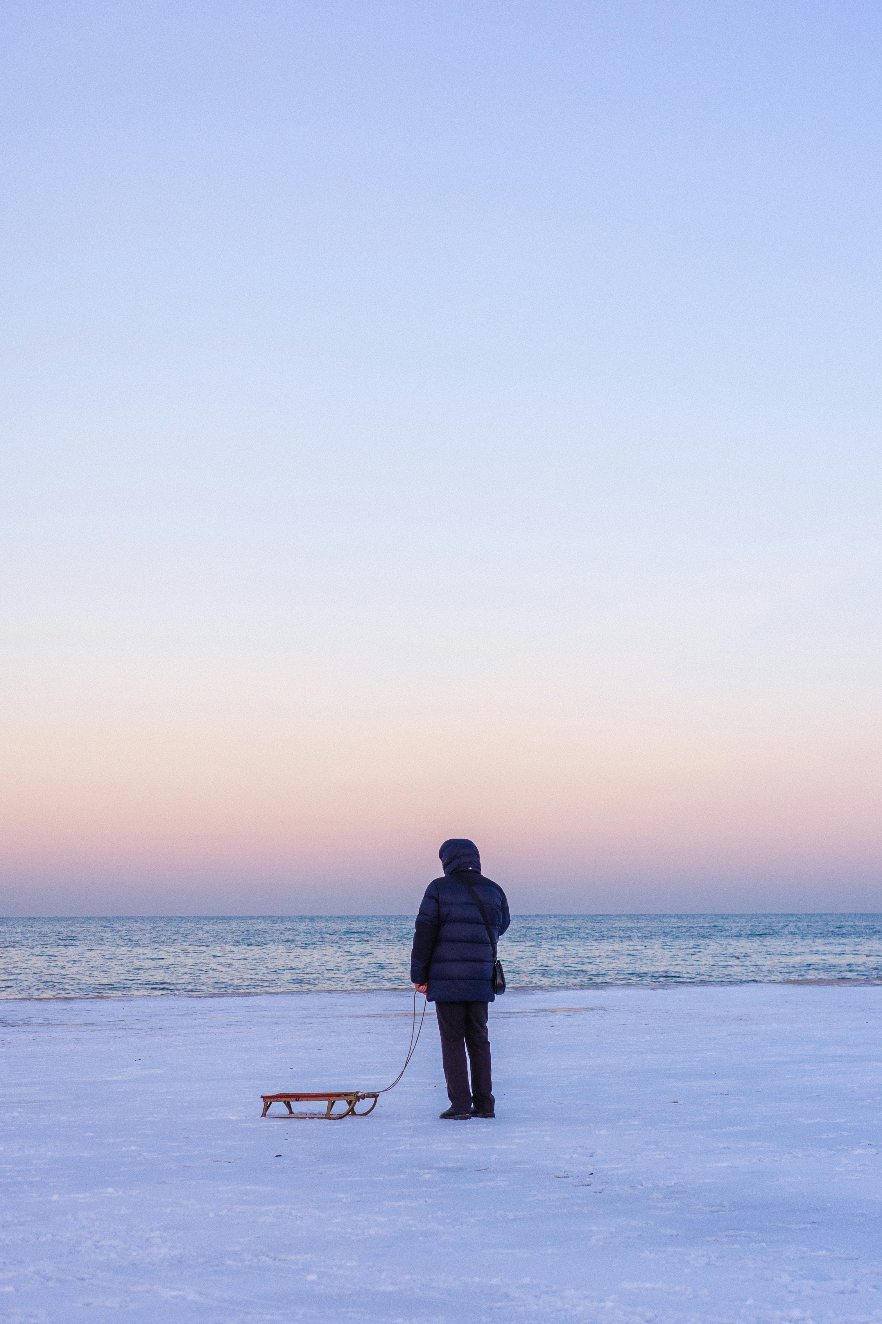 Person with sled on snowy beach at sunset
