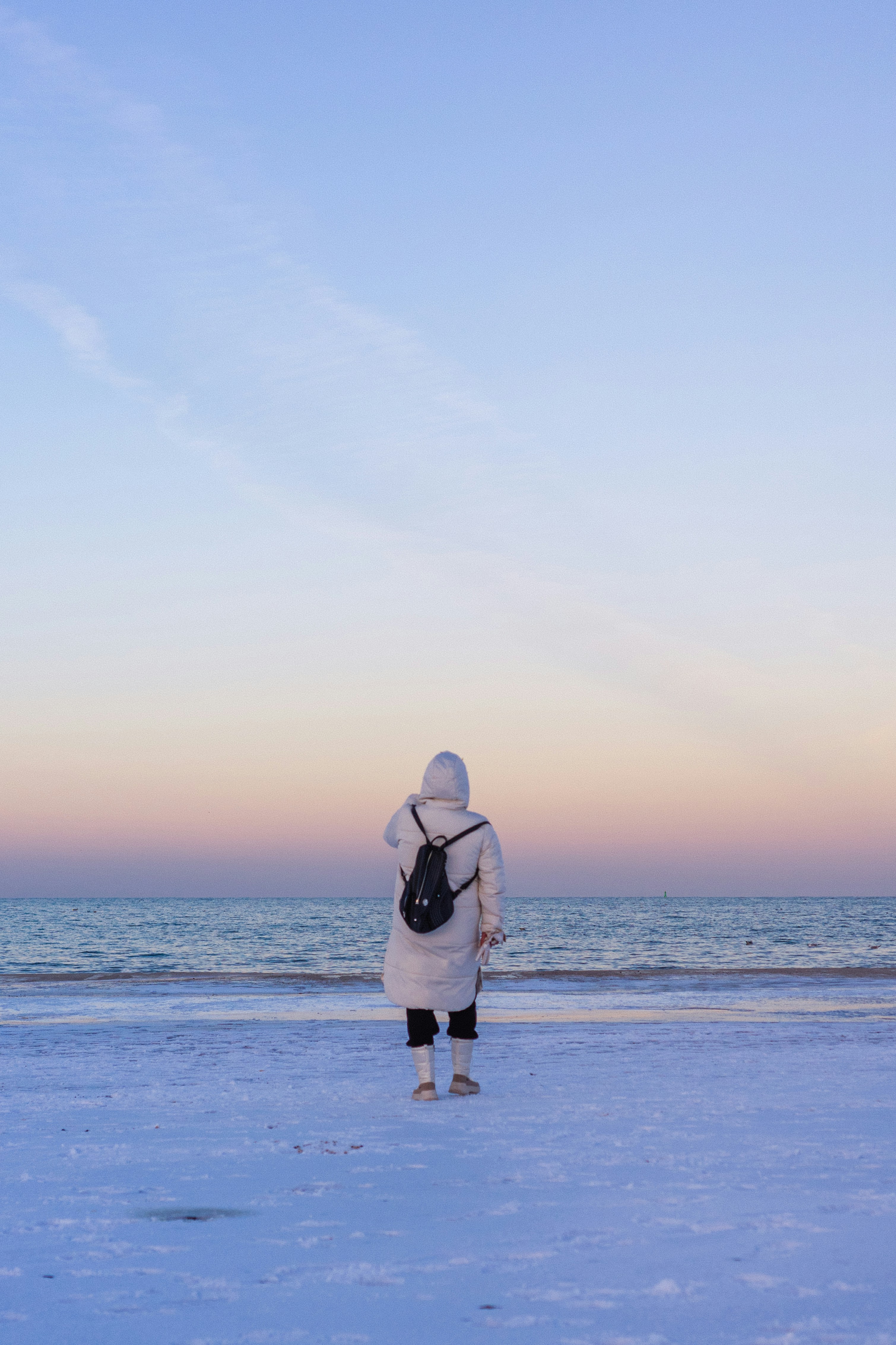 Woman in winter coat watches sunset over the ocean.