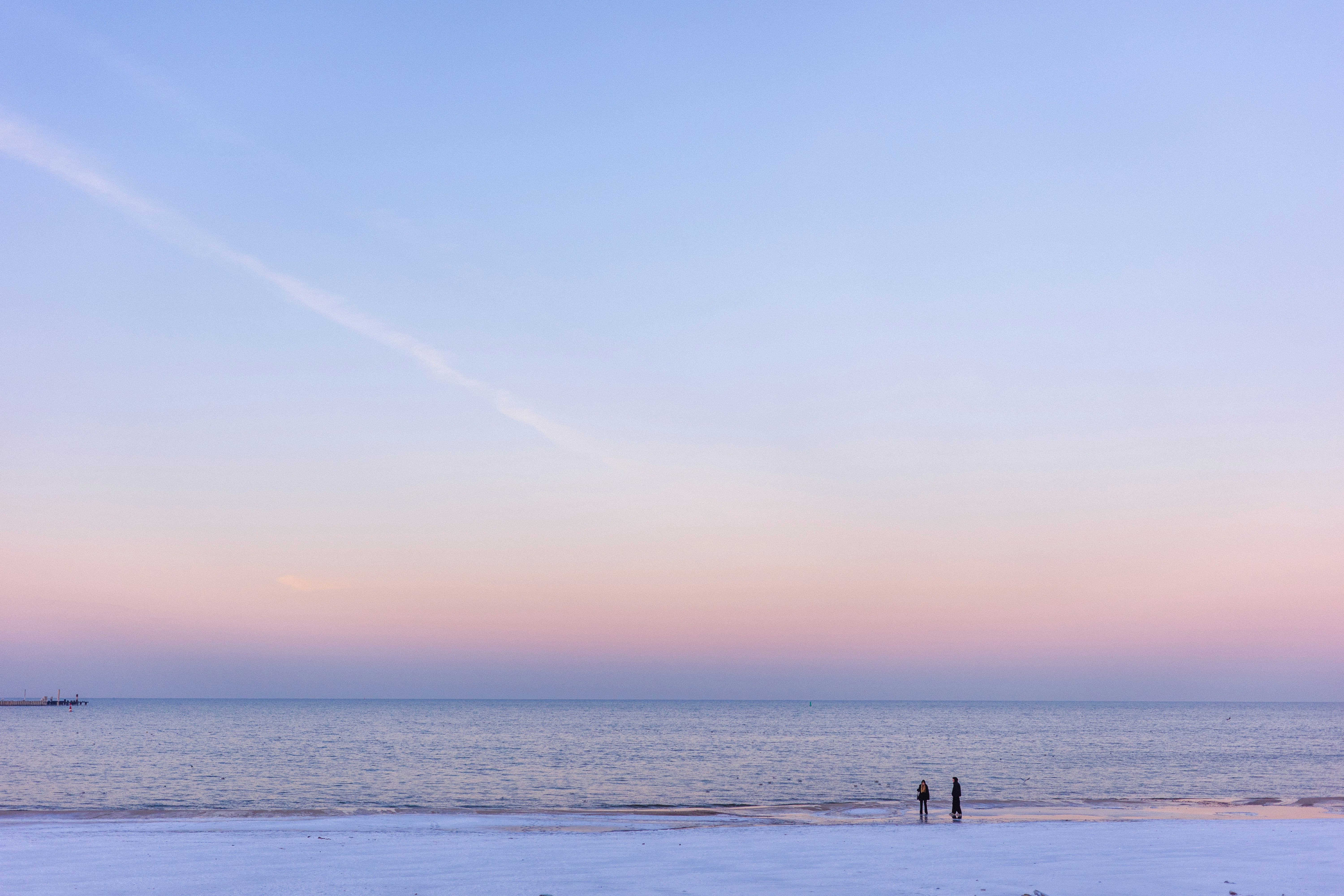 Two people stand on a snowy beach at sunset.