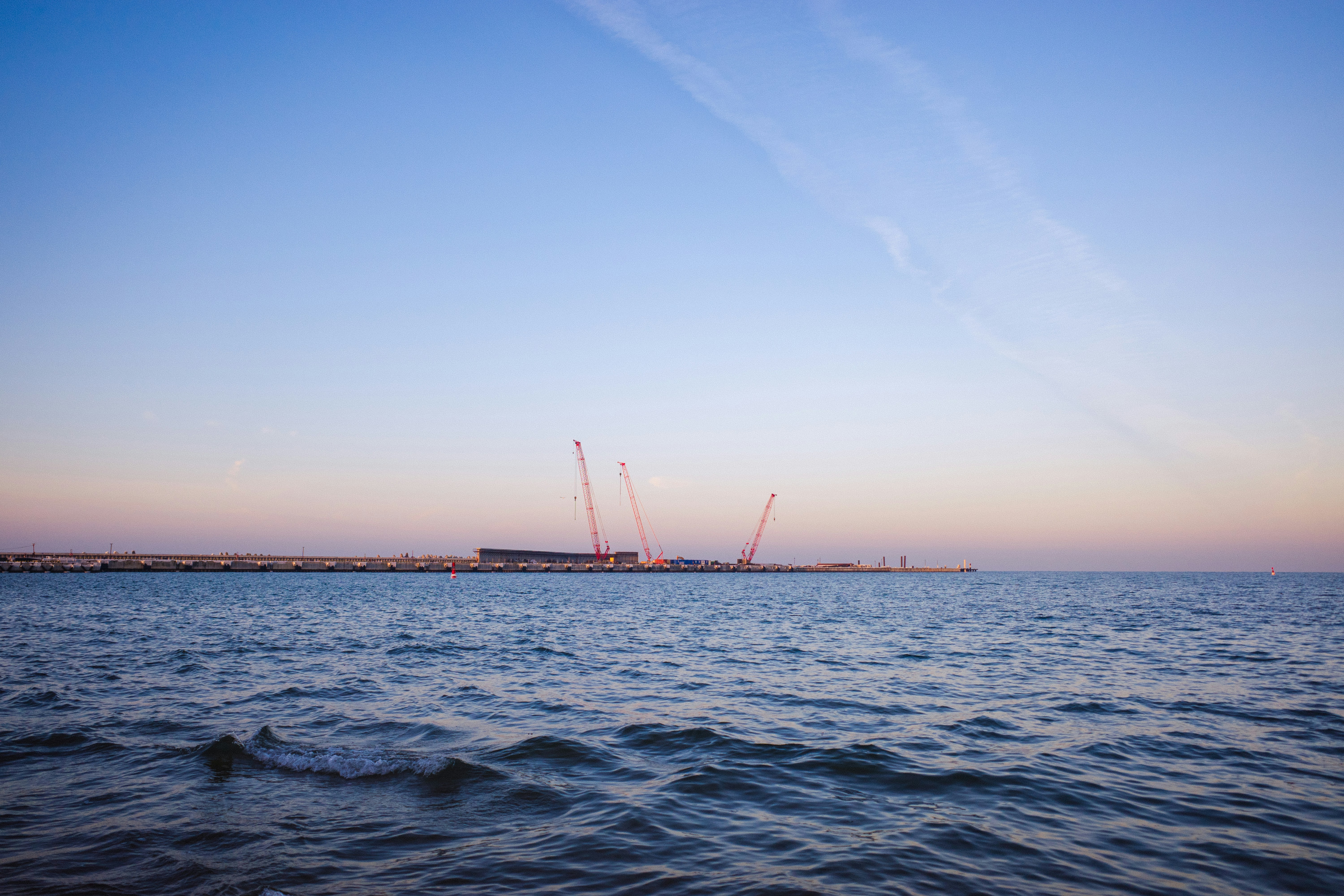 Construction cranes over the water at sunset