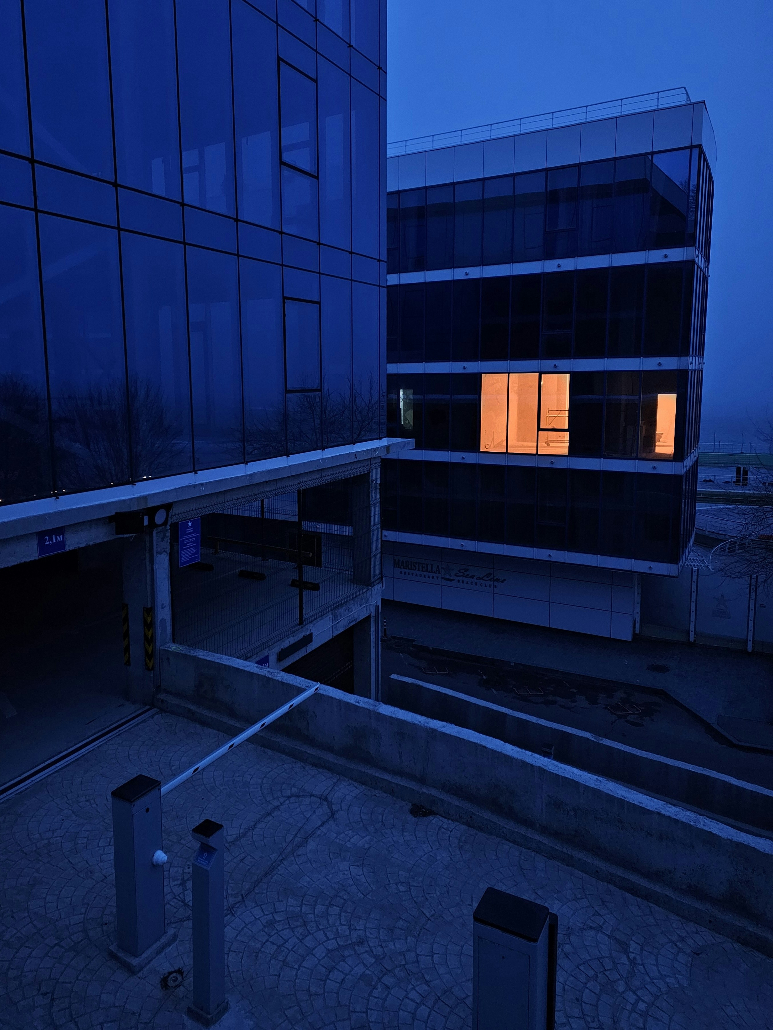 Modern glass buildings at dusk with one lit window.