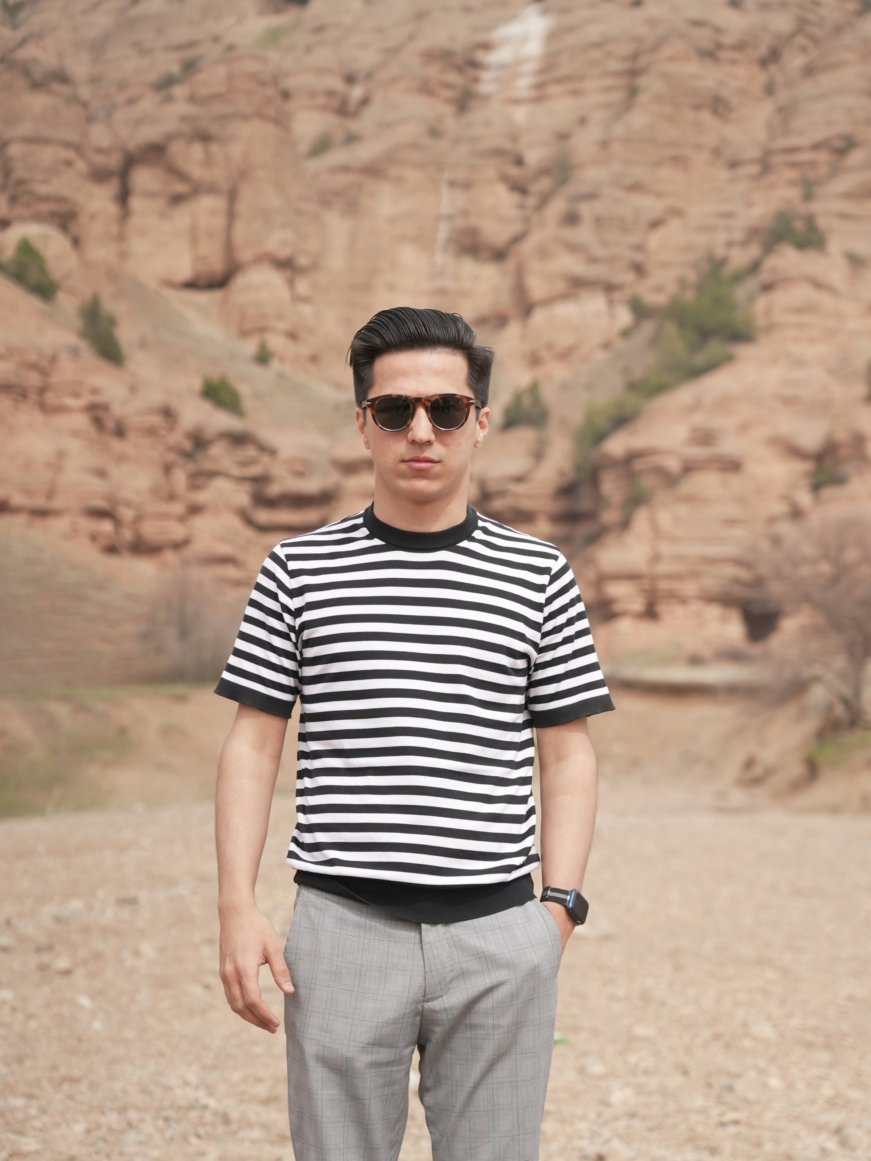 Man in striped shirt stands in a rocky, outdoor setting
