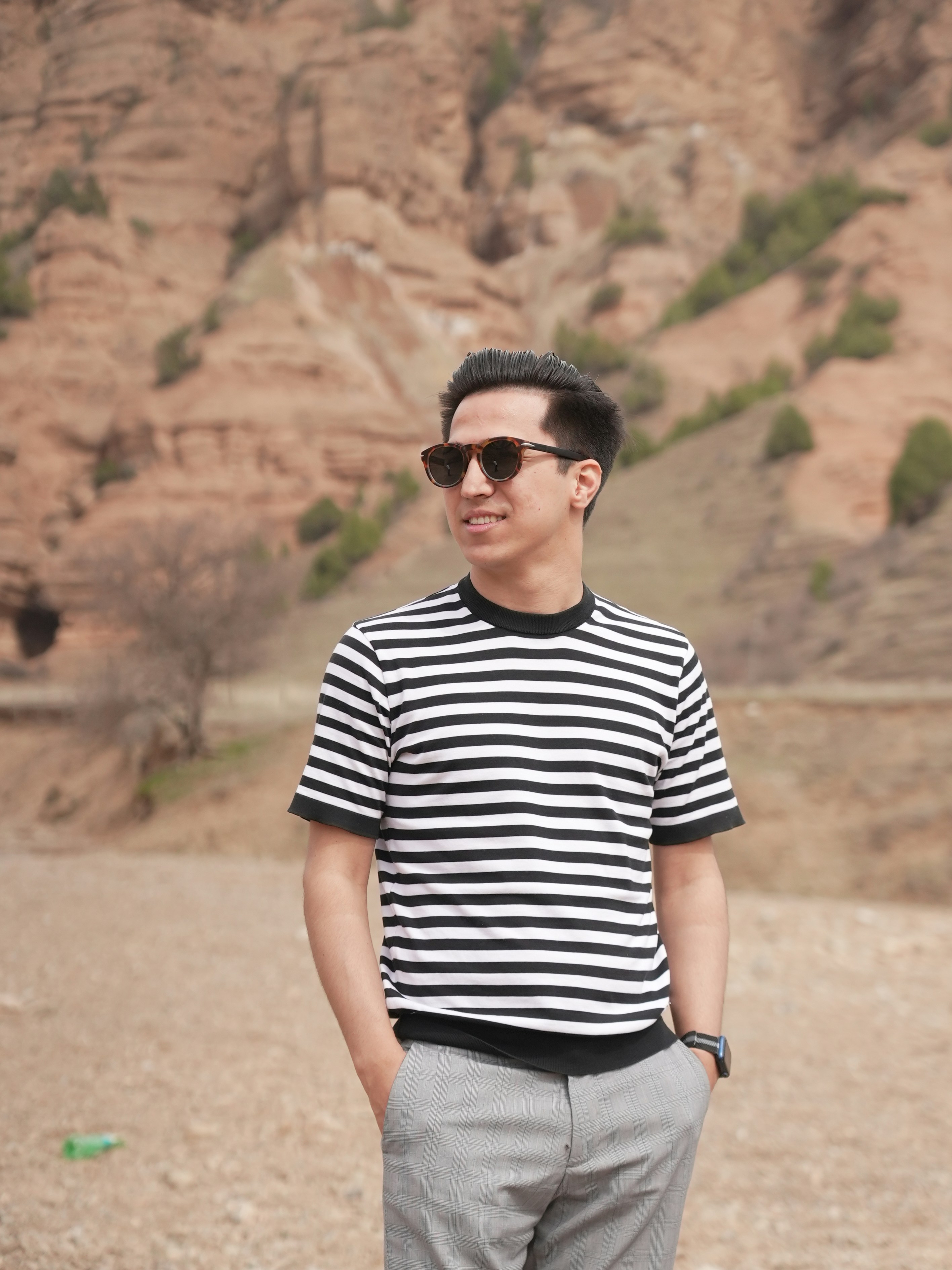 Man in striped shirt standing outdoors with hands in pockets.