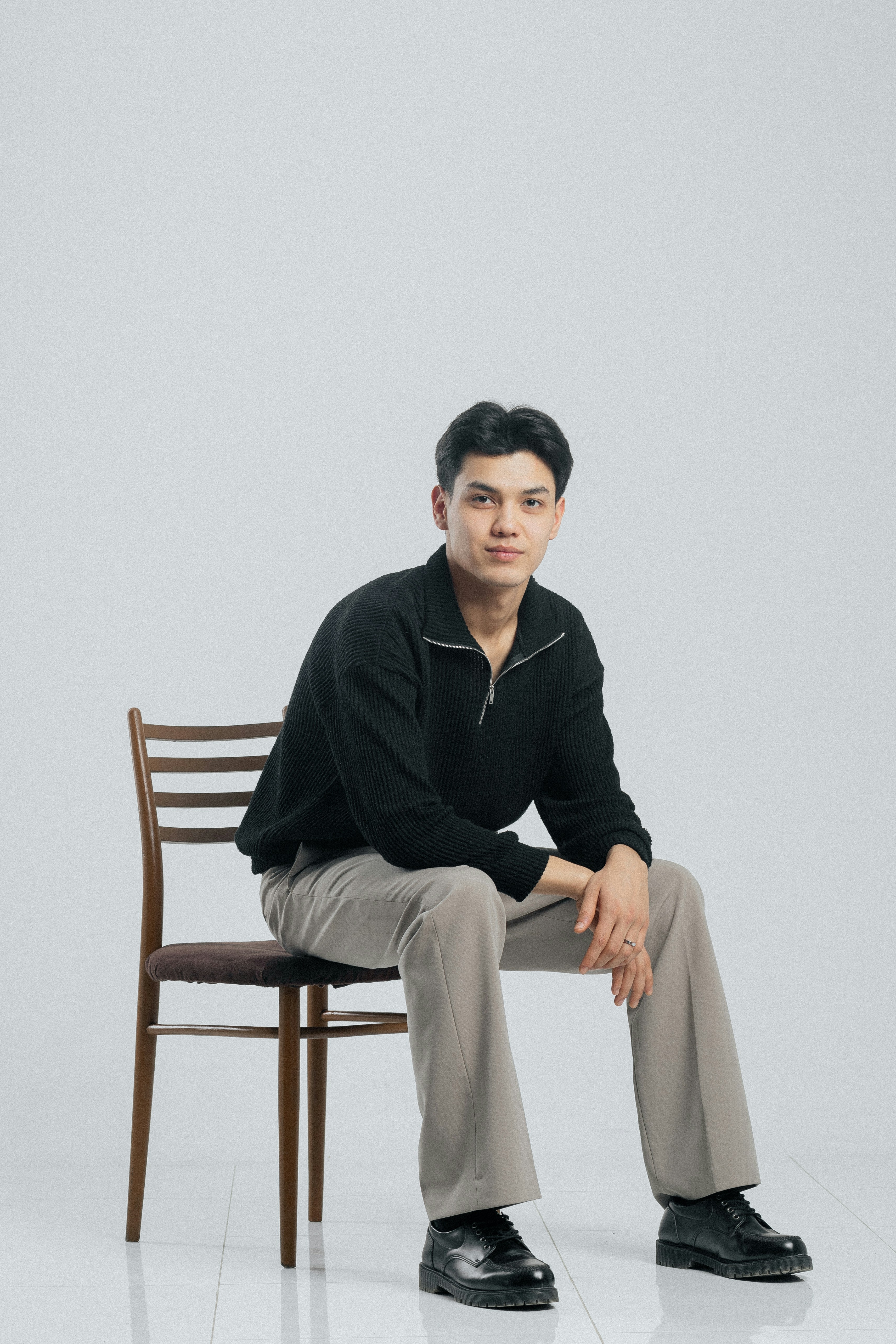 A young man in casual clothing sits on a chair.