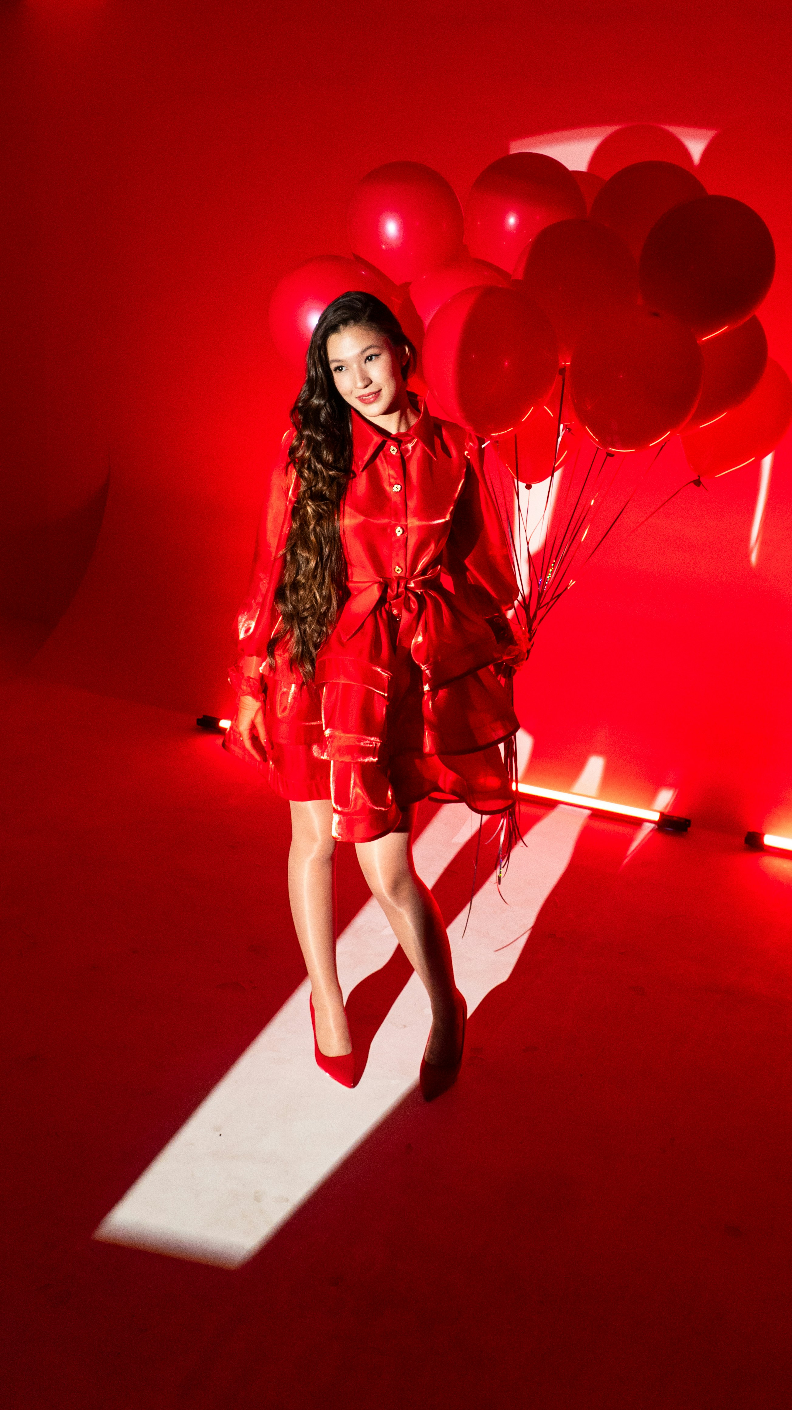 Woman in red dress holding red balloons on red background