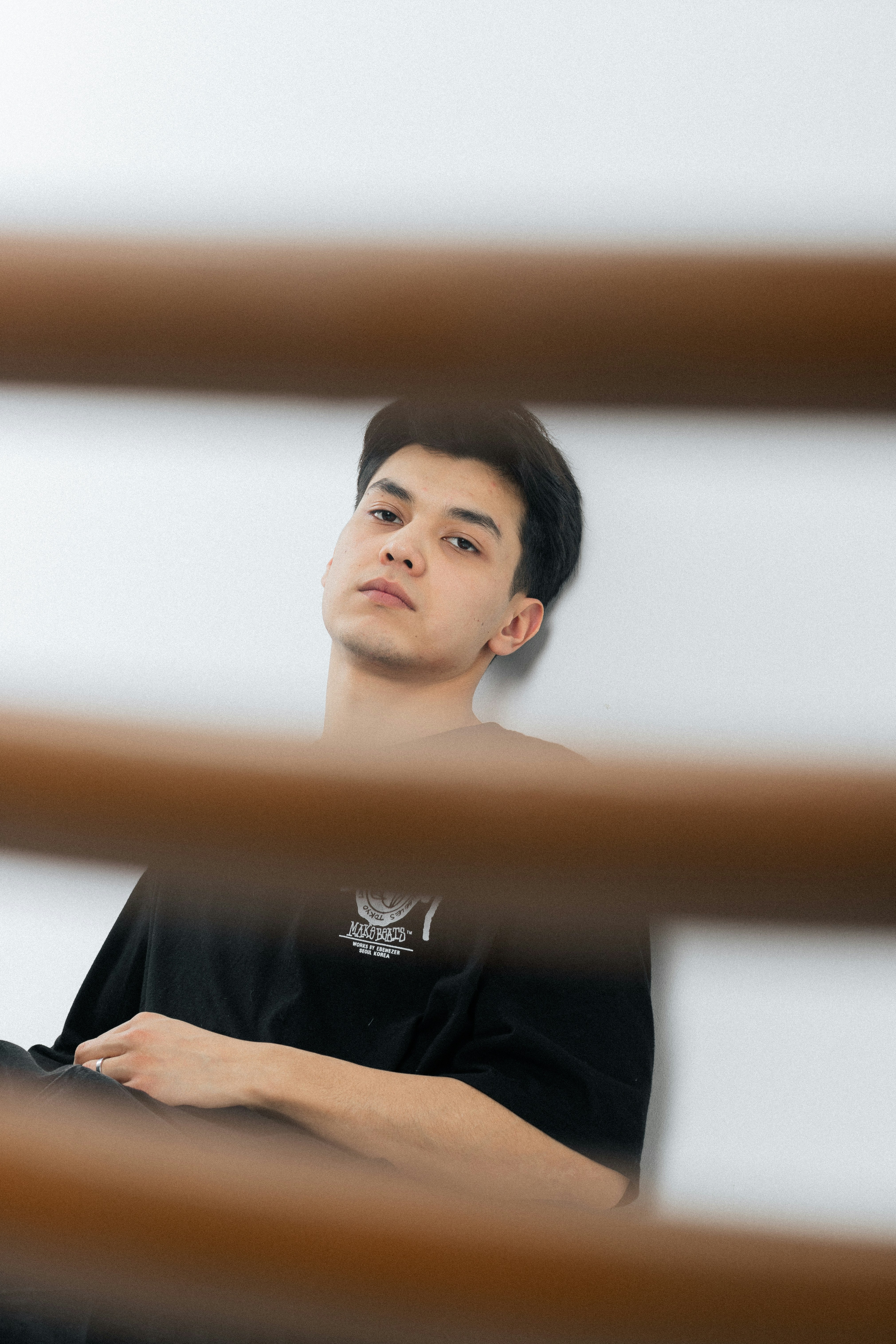 Young man in black t-shirt leaning against white wall.