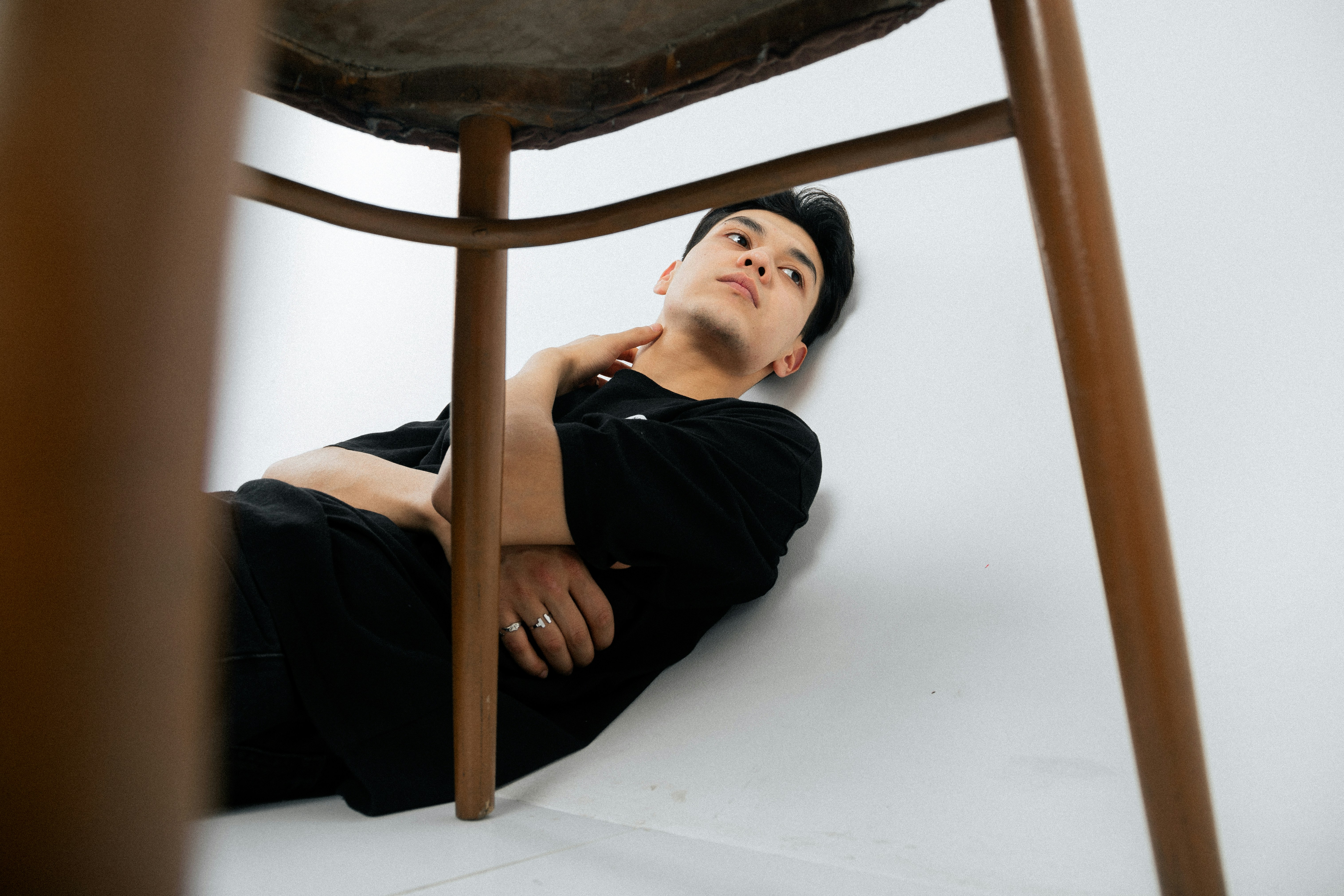 Young man lying on white floor under chair