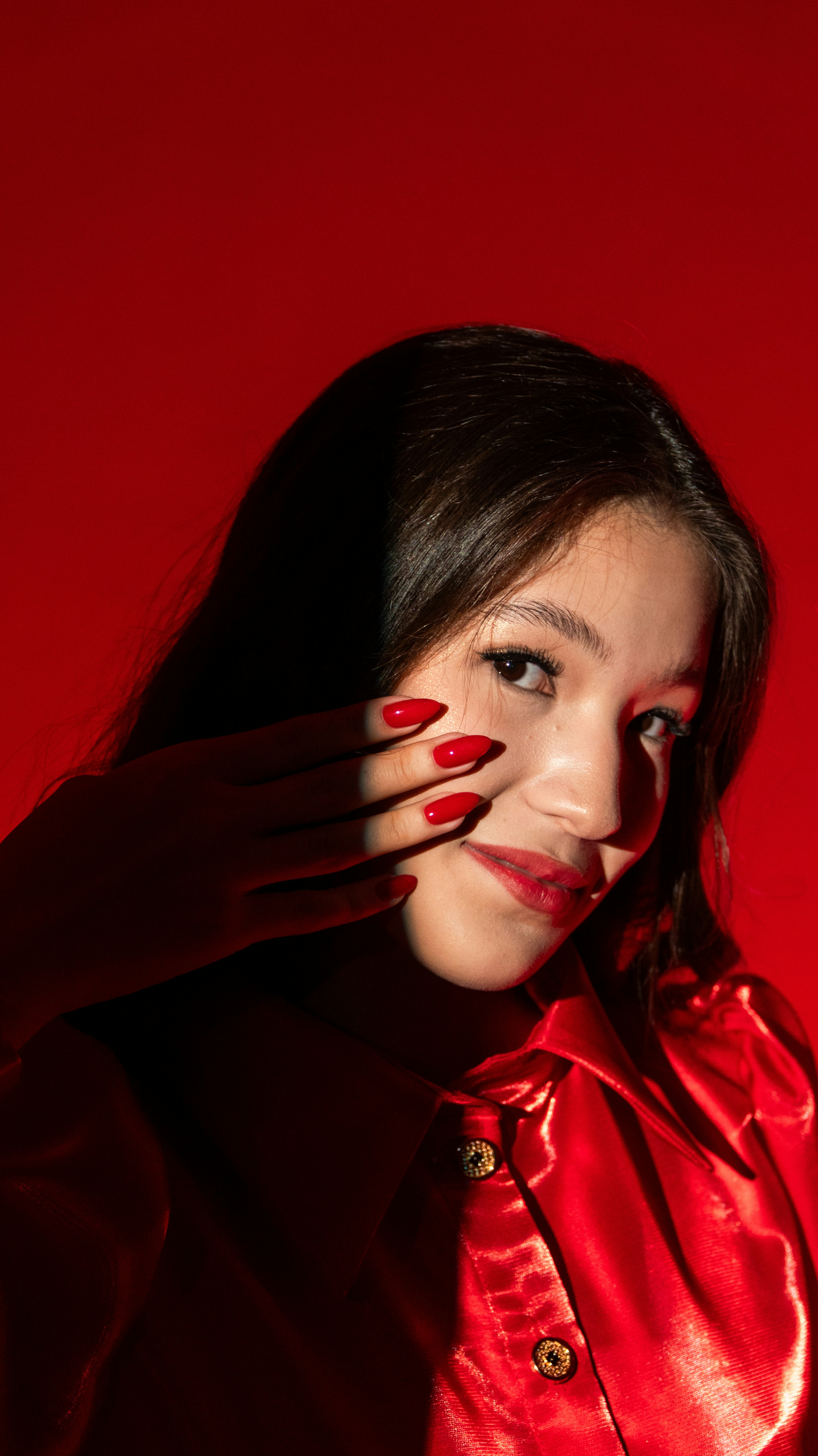 Woman with red nails and red shirt in dramatic lighting.