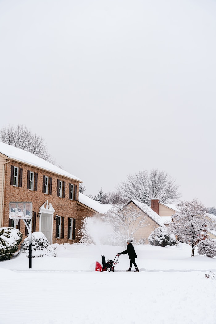 Snow removal — person using snow blower in front of house