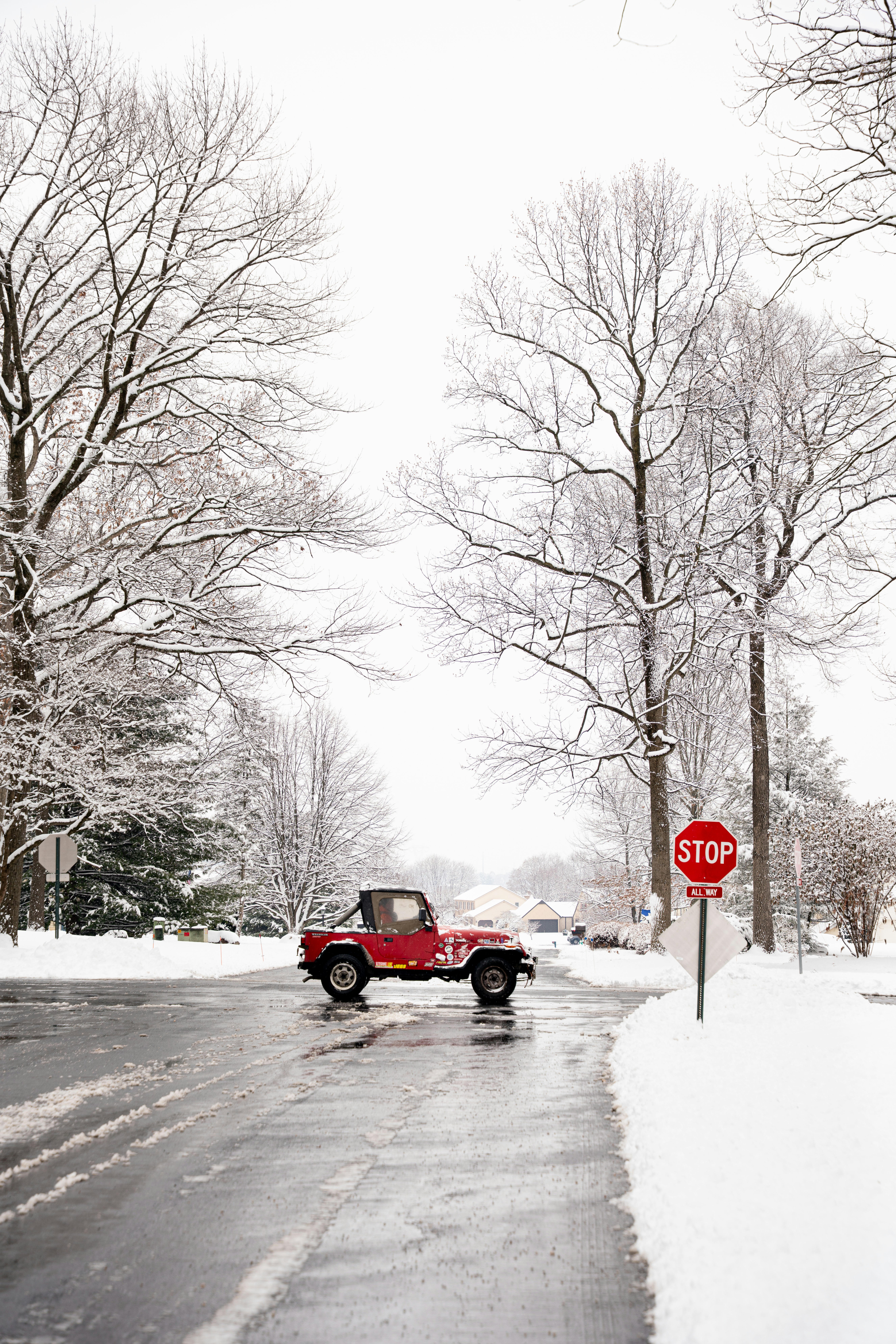 Red jeep driving on a snowy street with stop sign