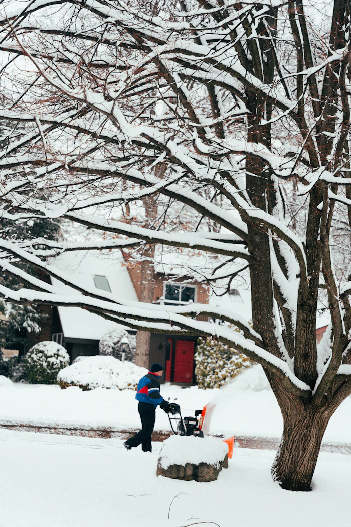 Person clearing snow in front of a house with a snow blower