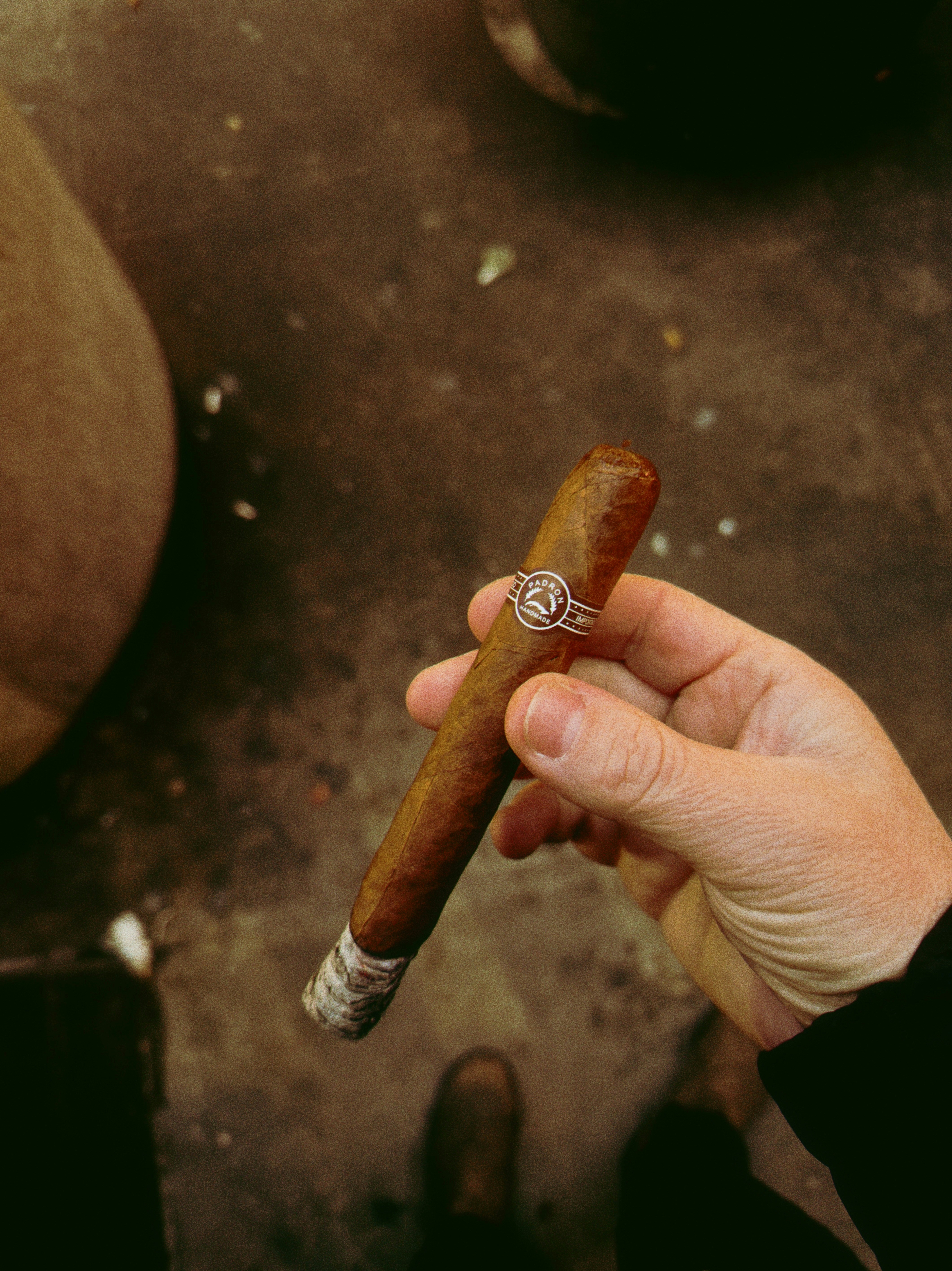 A hand holds a lit cigar with a silver band.