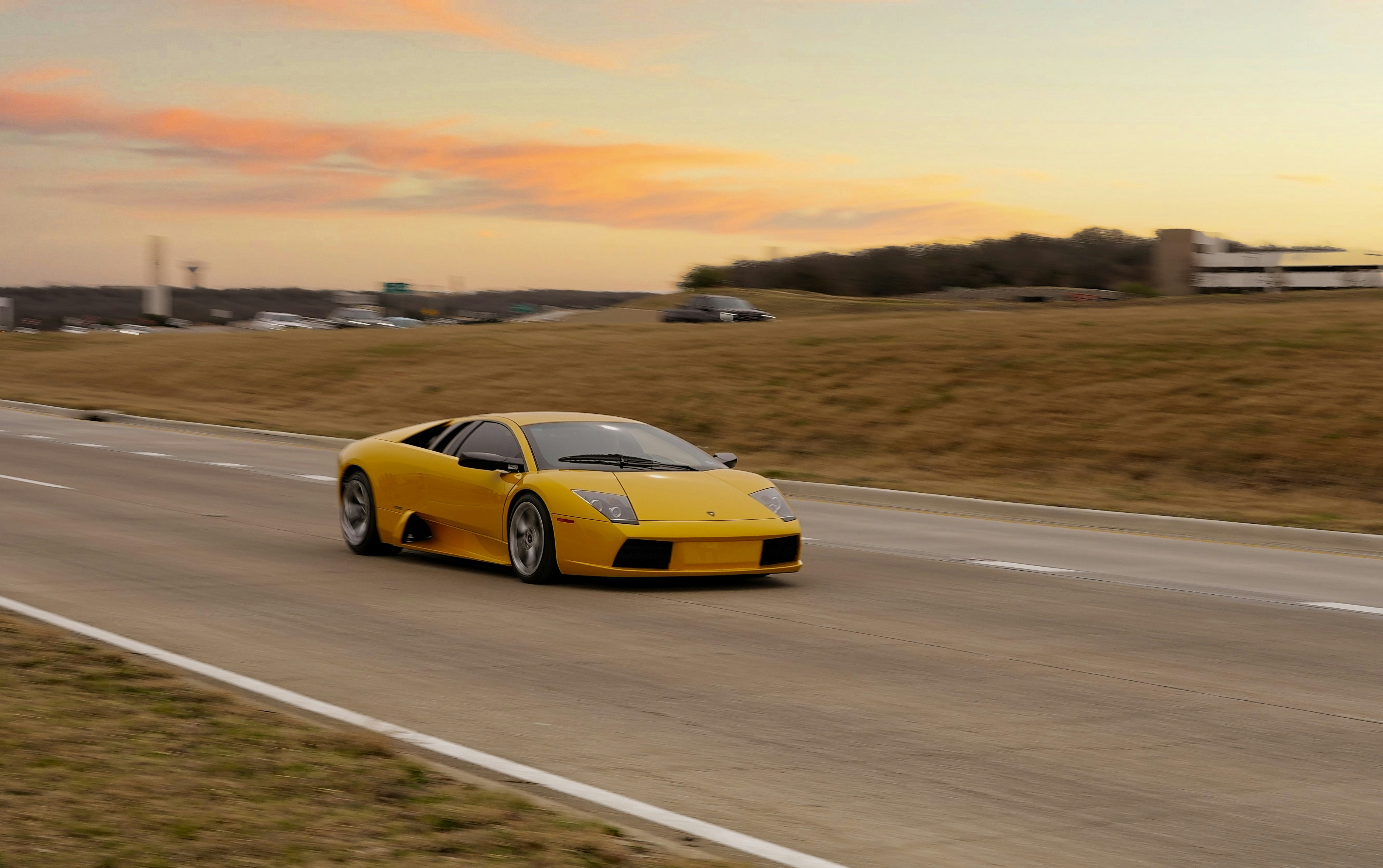 A yellow sports car drives on a highway at sunset.