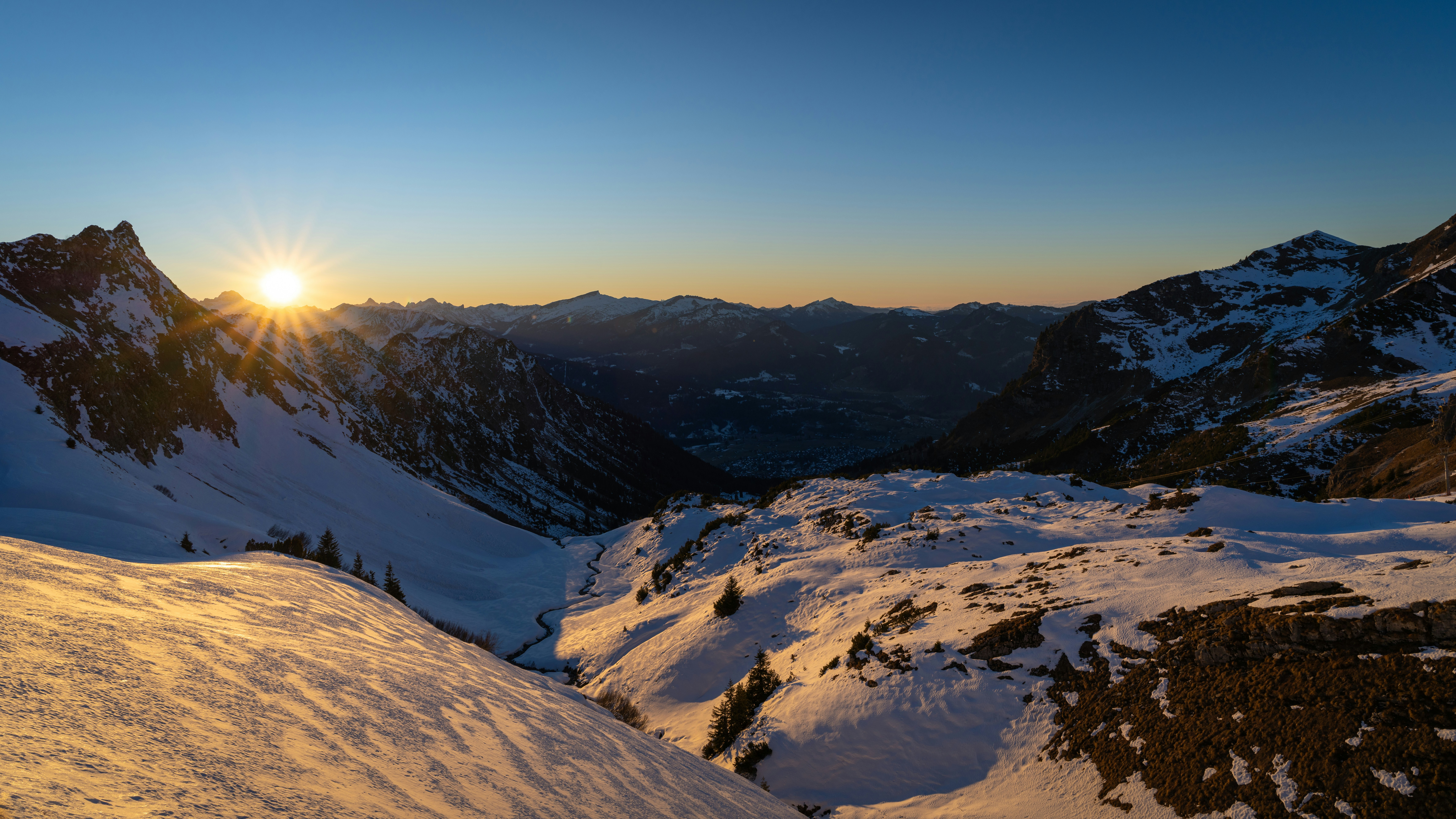 Sonnenaufgang über einem schneebedeckten Bergtal.