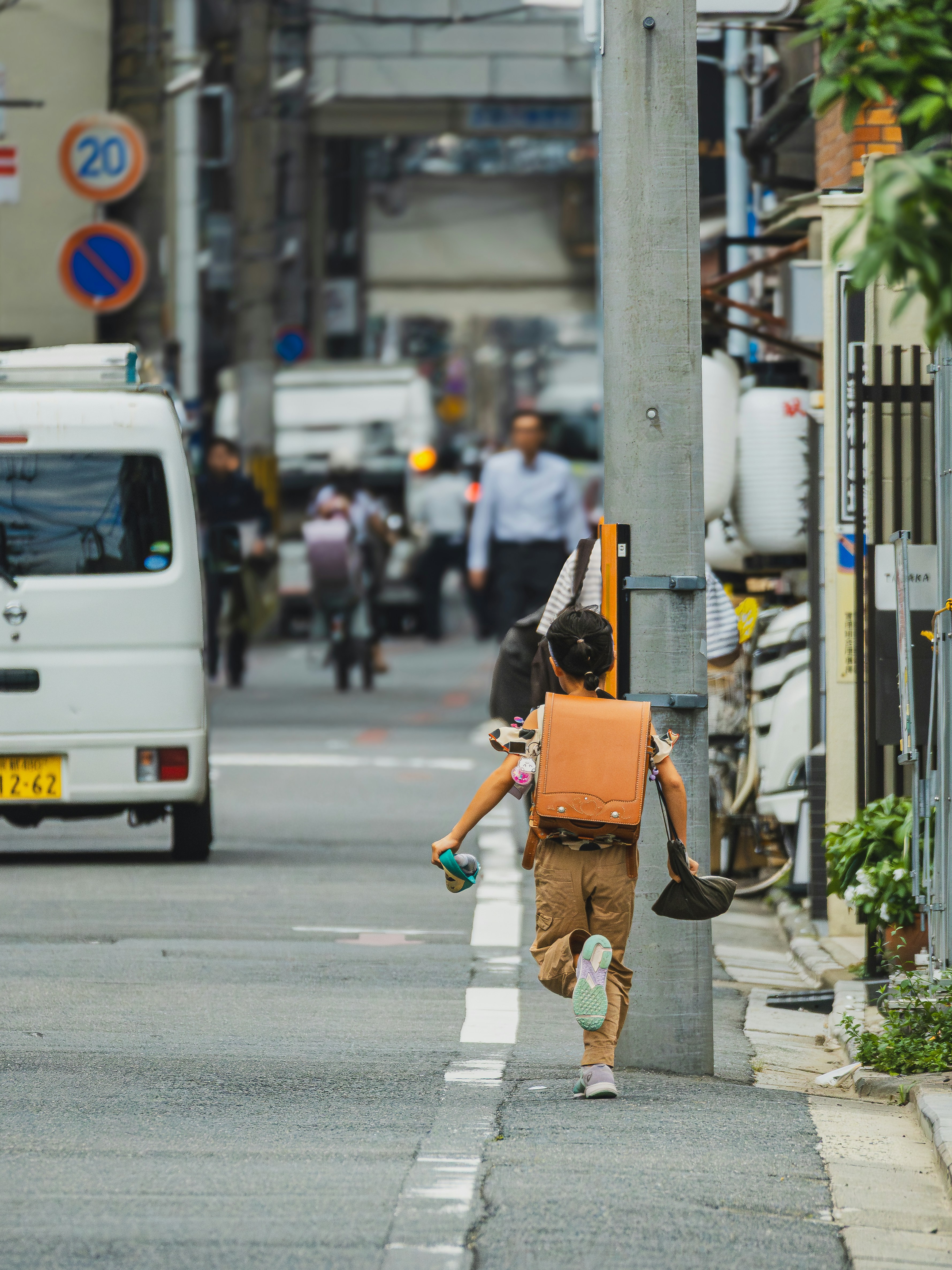 Child with backpack runs down a city street.
