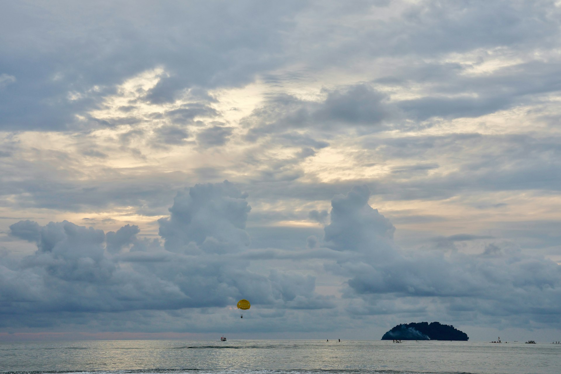 A yellow parachute floats over the ocean near an island.