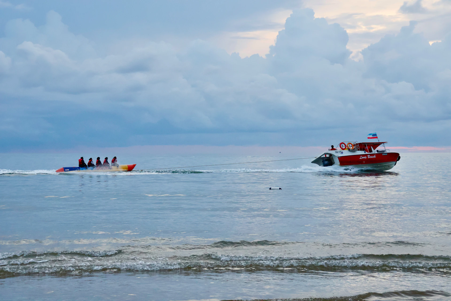 People riding a banana boat towed by a speed boat