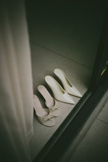 Two pairs of elegant white heels on floor.