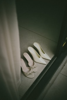 Two pairs of elegant white heels on floor.