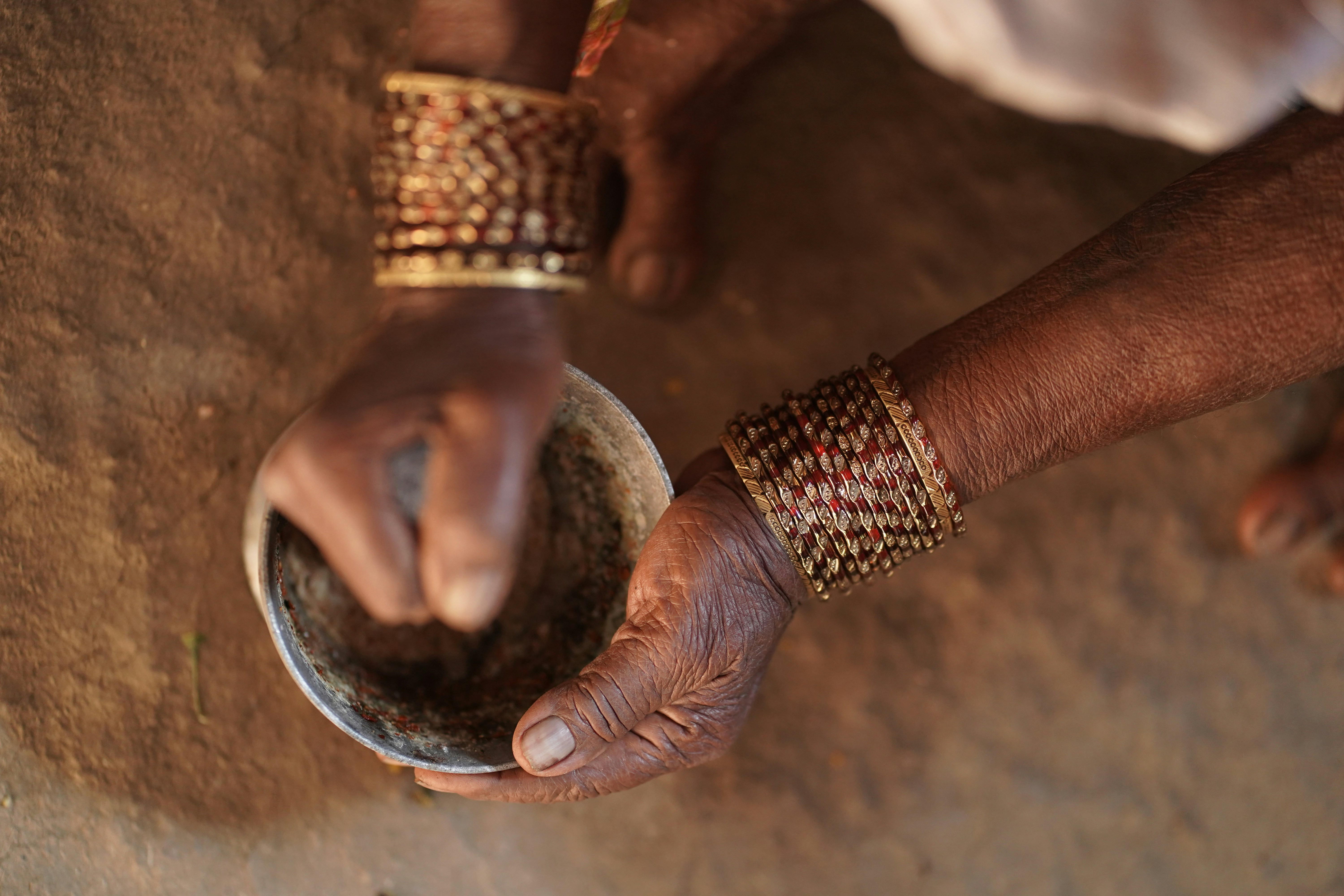 Hands grinding spices in a bowl with bracelets.