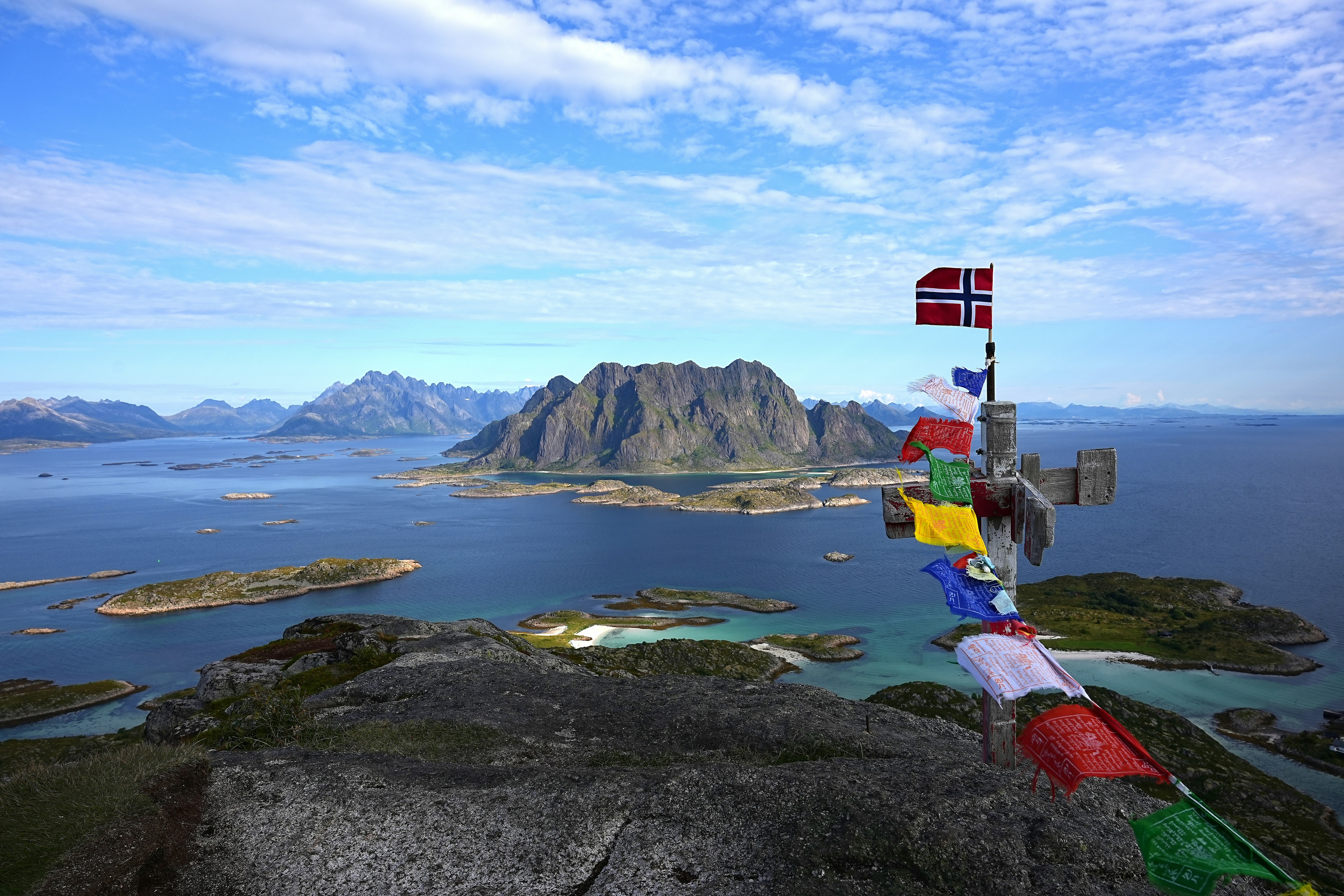 Norwegian flag and prayer flags on mountain overlooking islands