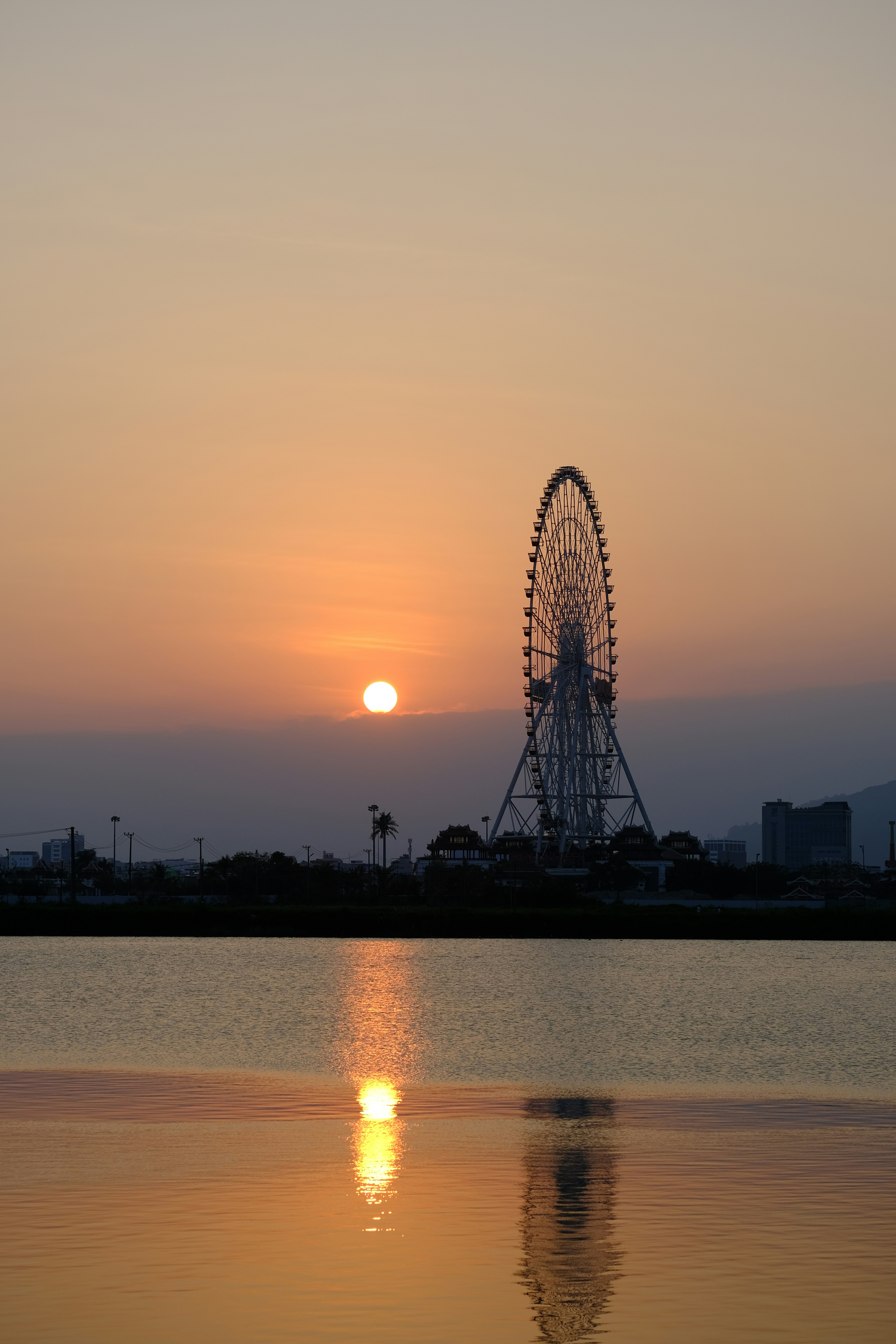 Ferris wheel silhouetted against a sunset over water