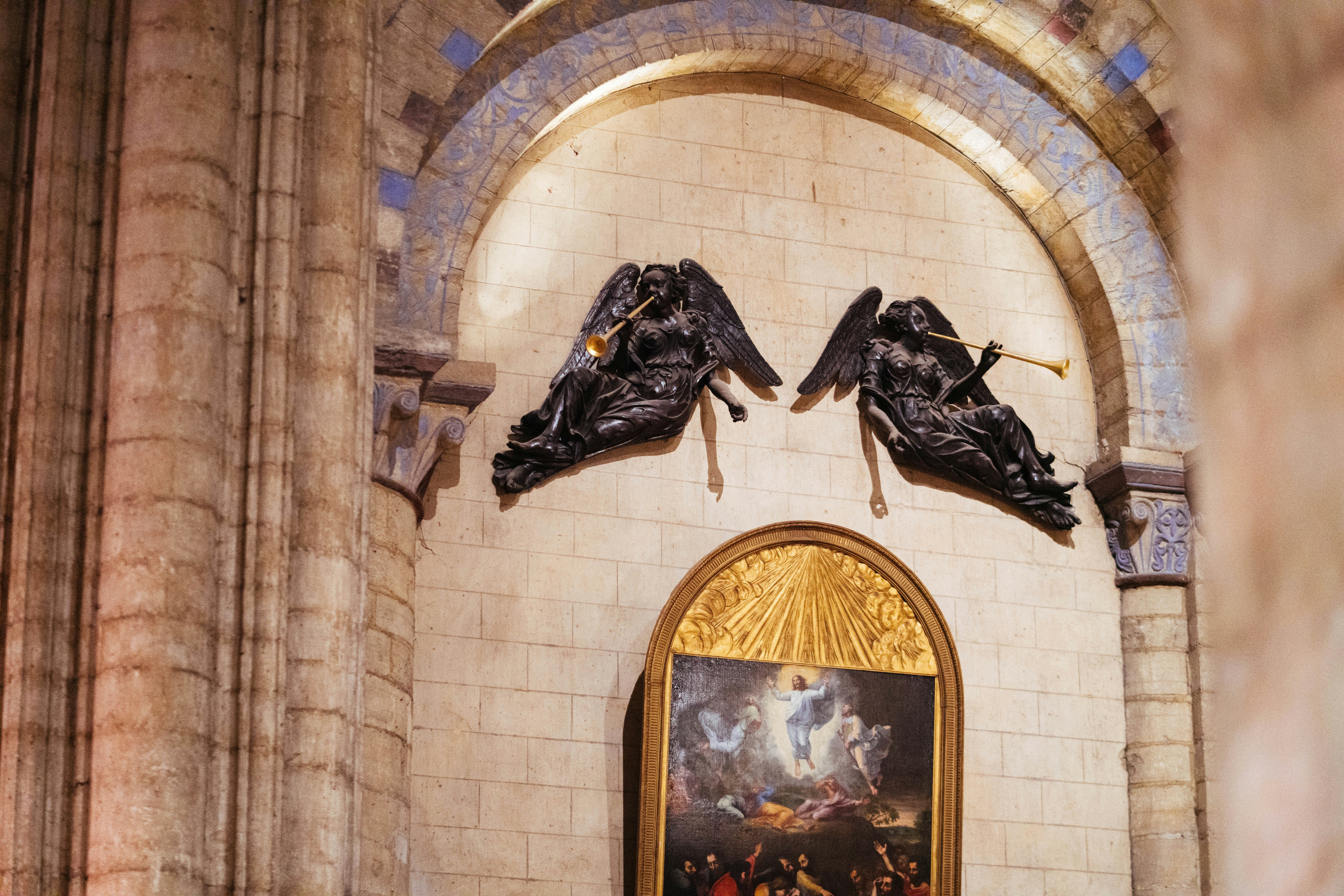 Dos ornamentadas esculturas de ángeles sobre una pintura religiosa.