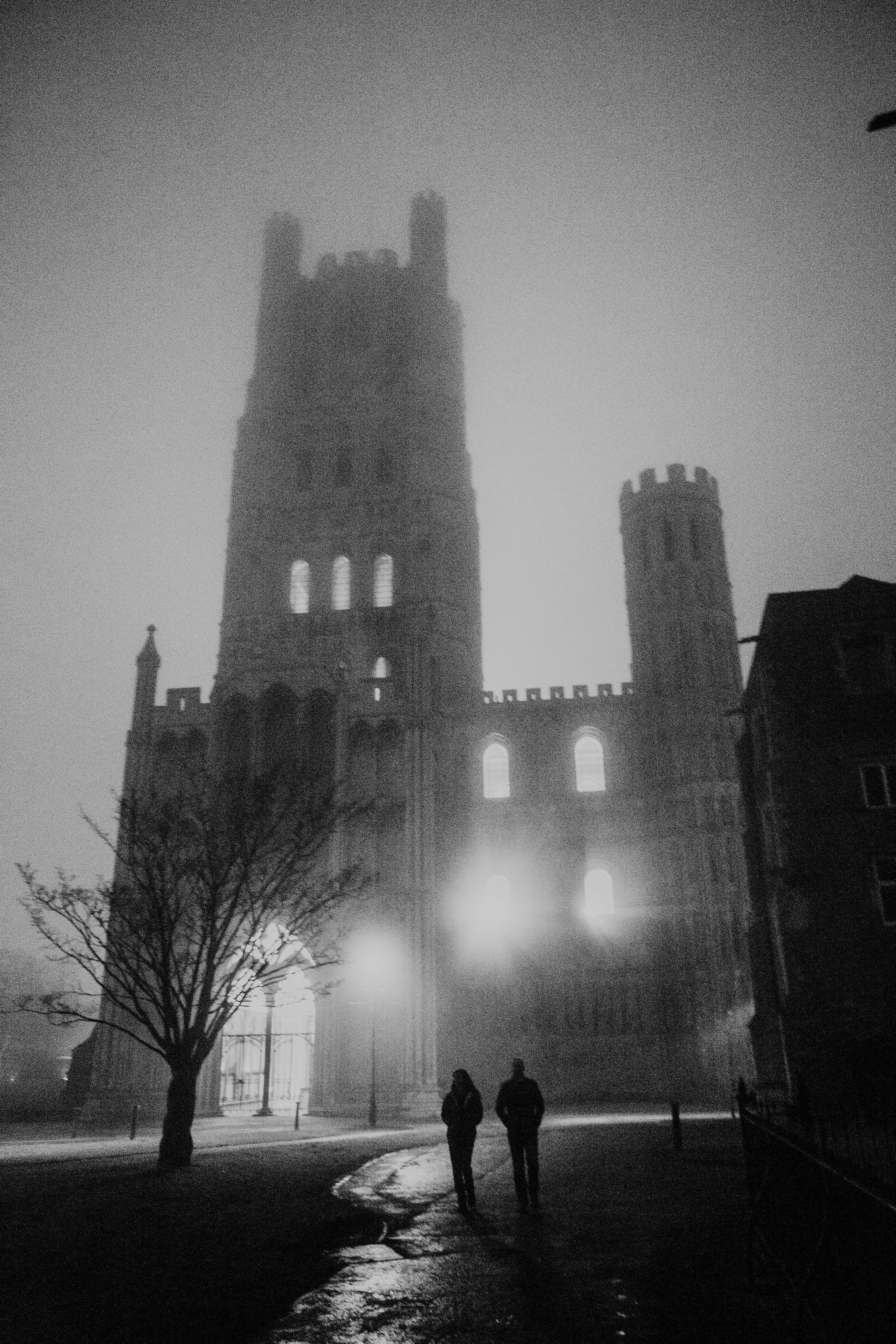 Two figures walk towards a large cathedral in fog.