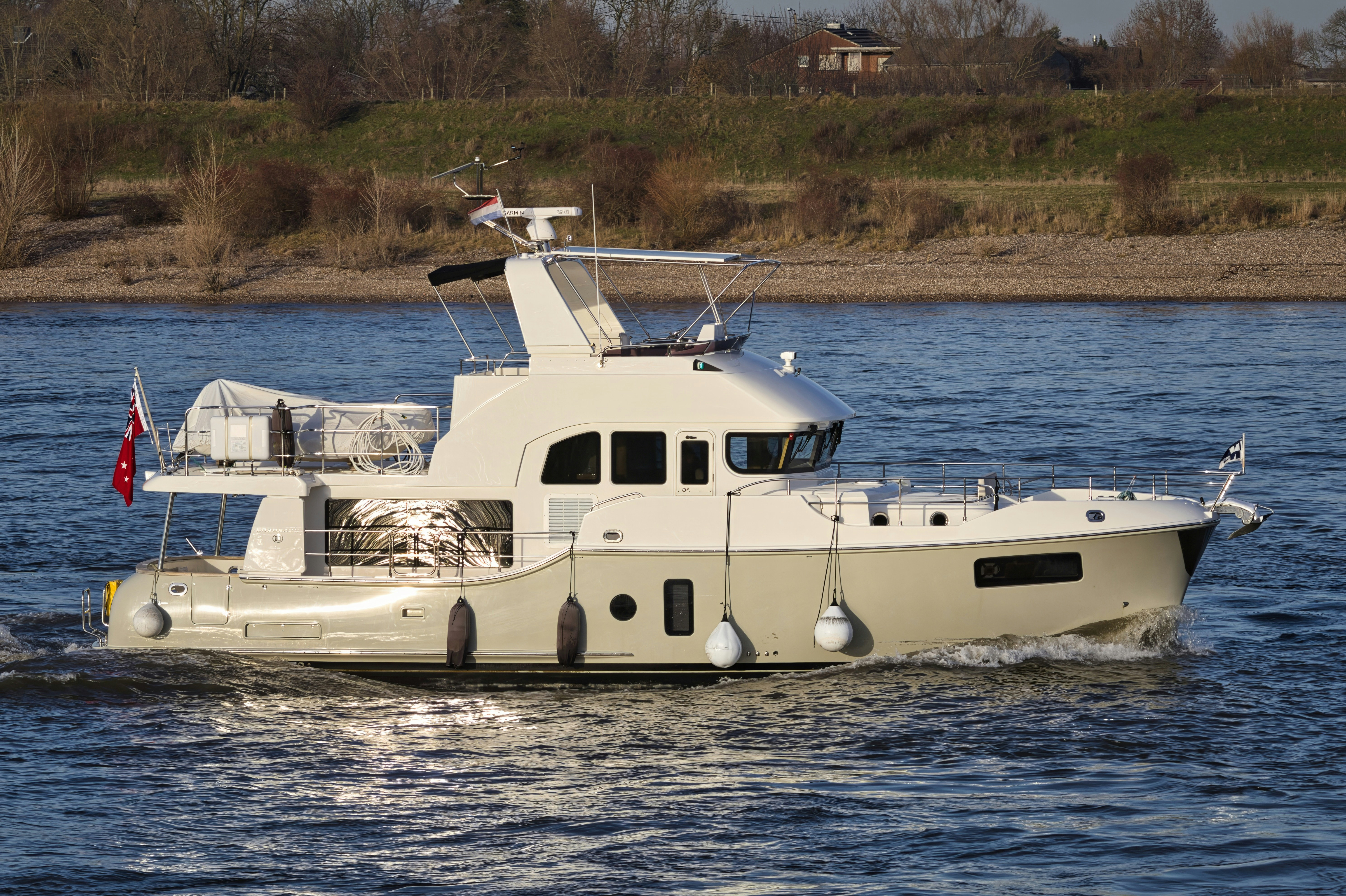 A modern yacht sails on a wide river.