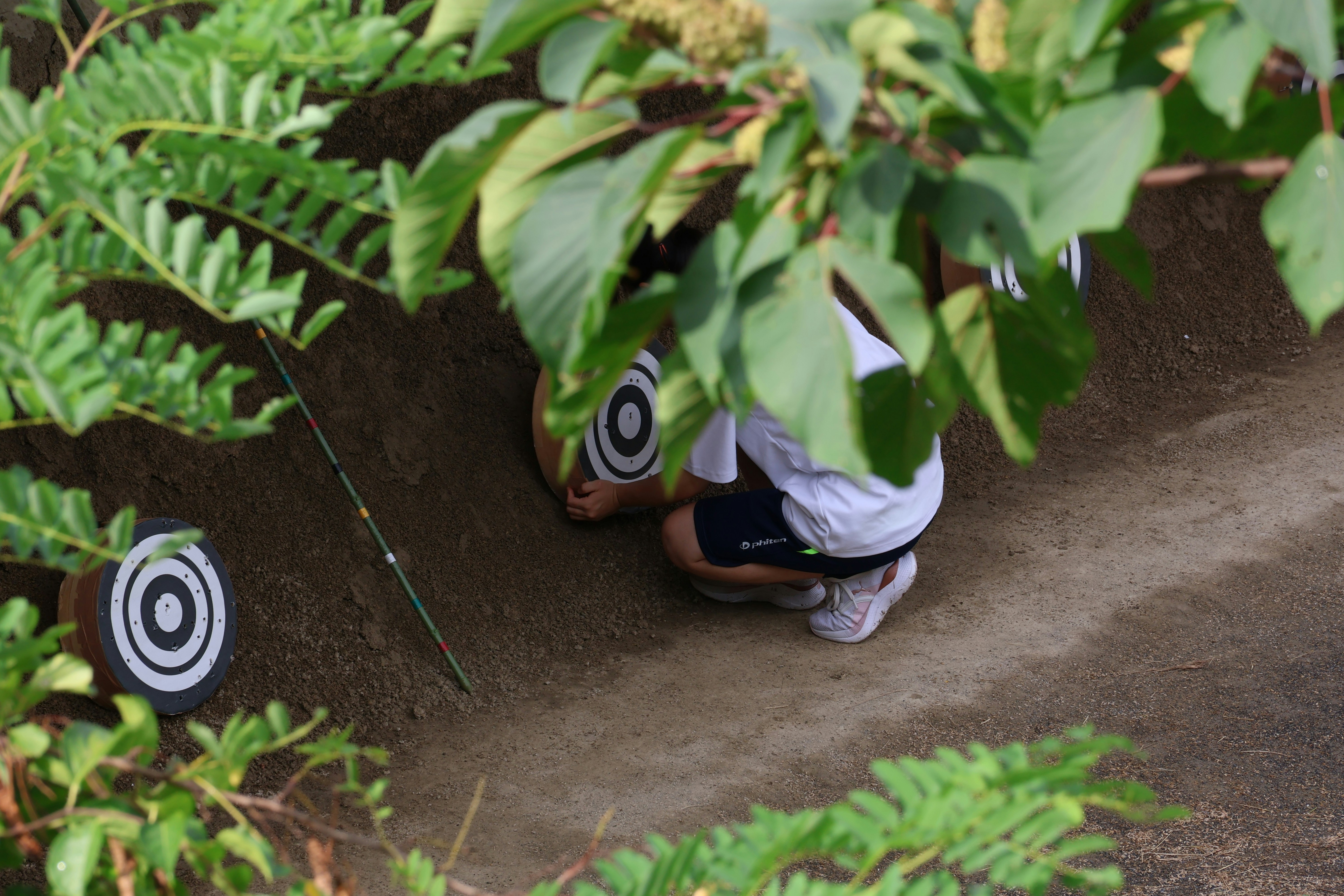 Archer crouching behind leaves aiming at targets