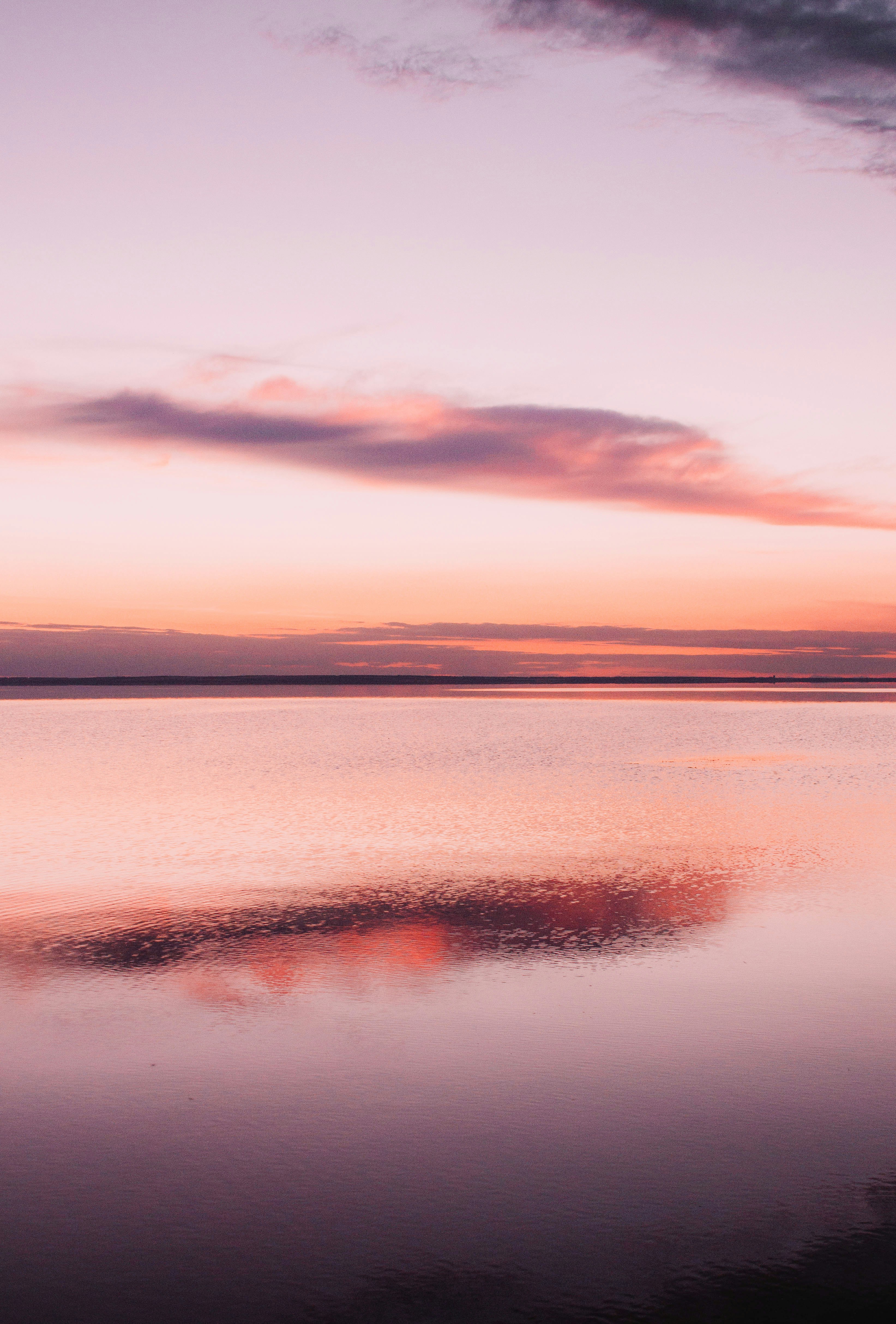 Calm water reflects a pastel sunset sky with clouds